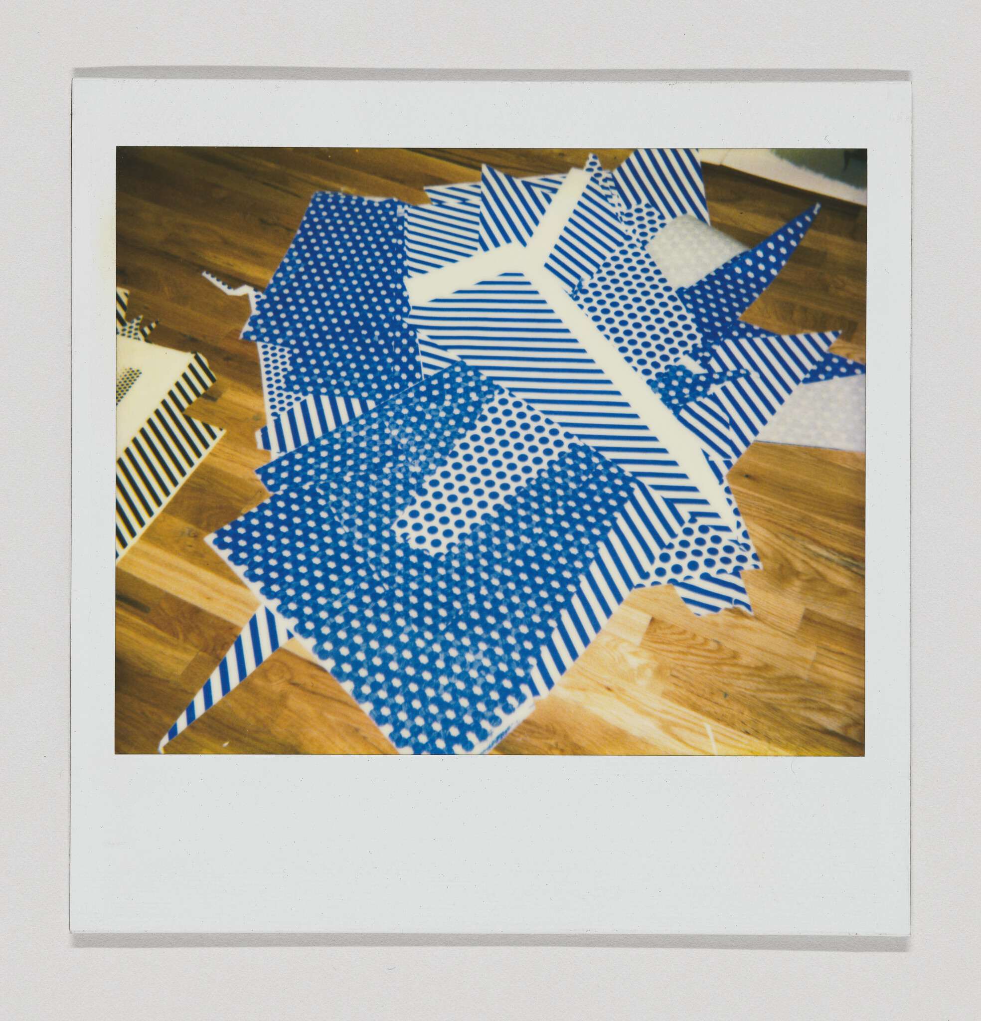 Several blue-and-white patterned paper sheets cut into geometric shapes scattered on a wooden floor.