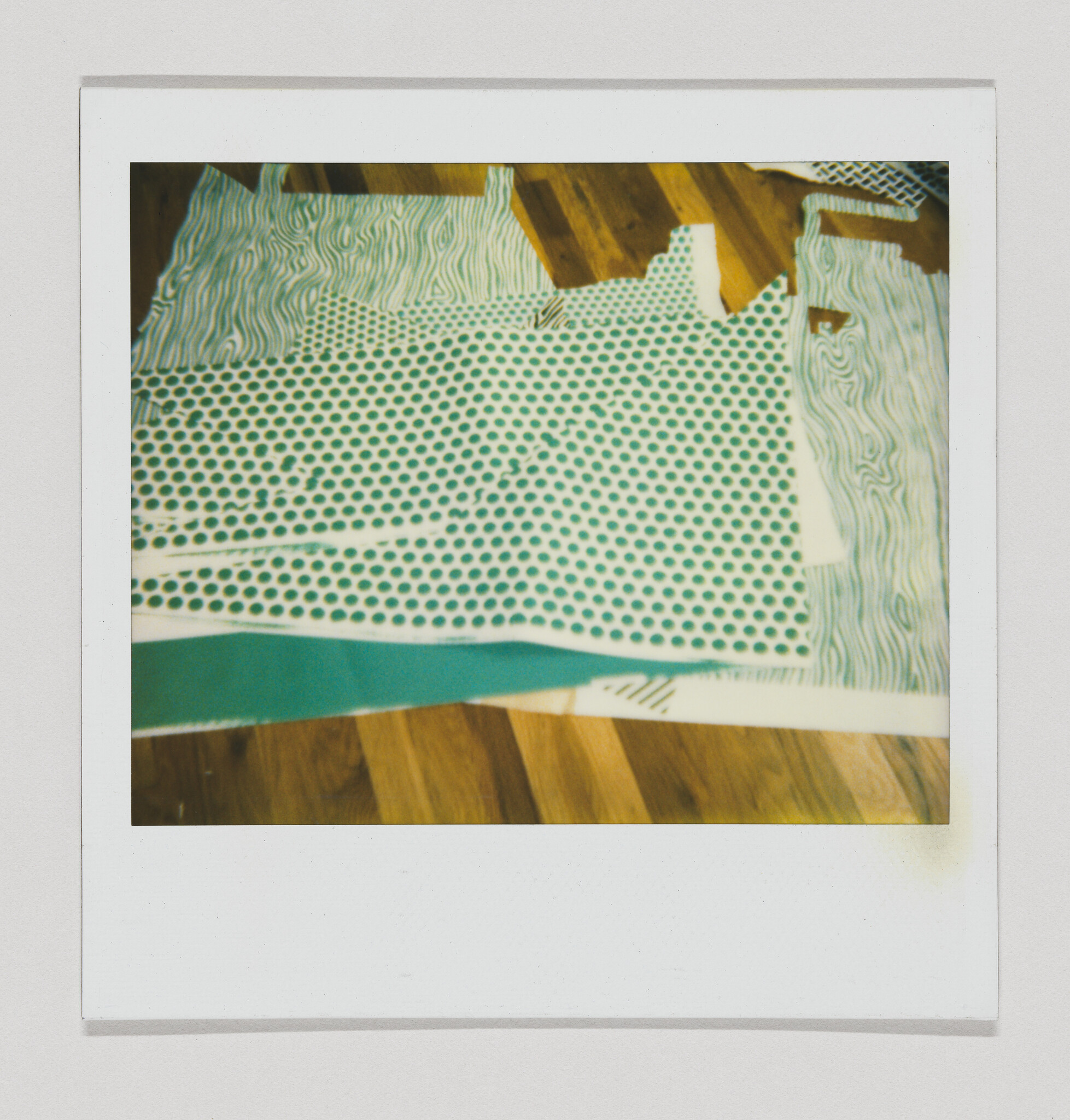 Several green polka dot and wavy striped fabric pieces laid out on a wooden floor.