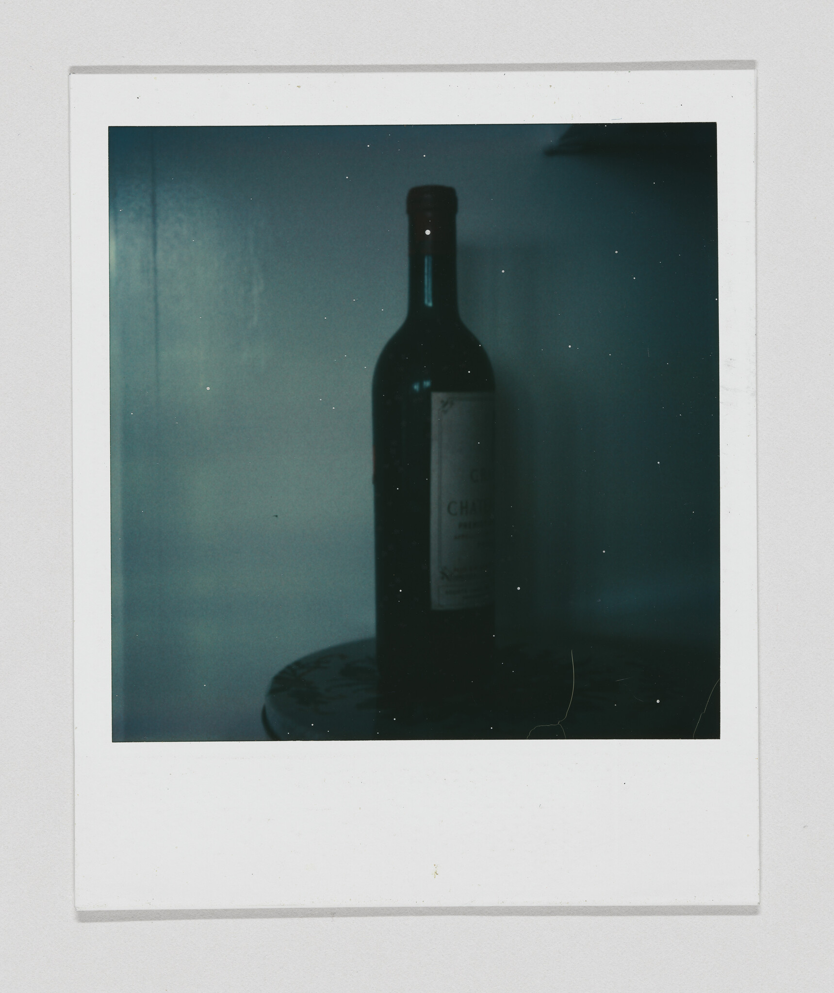 A dark wine bottle sits on a small round table against a dimly lit wall.