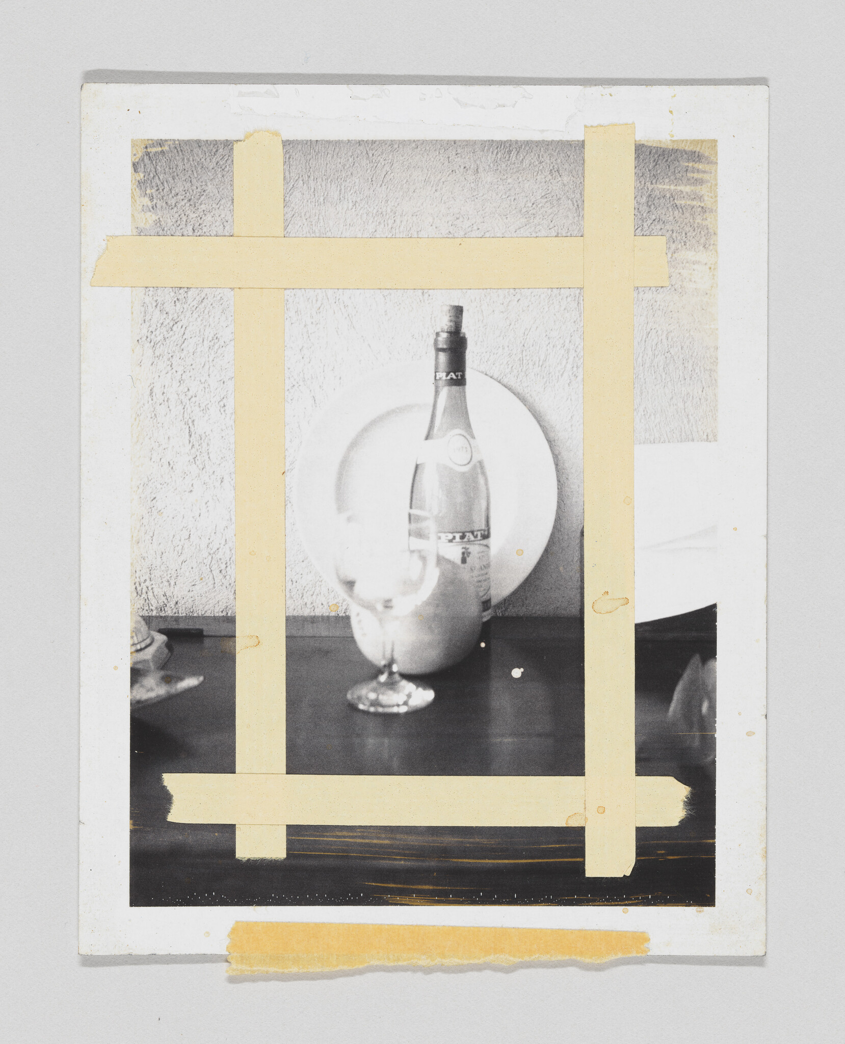 A wine bottle, empty glass, and plate sit on a table framed by crossed masking tape.