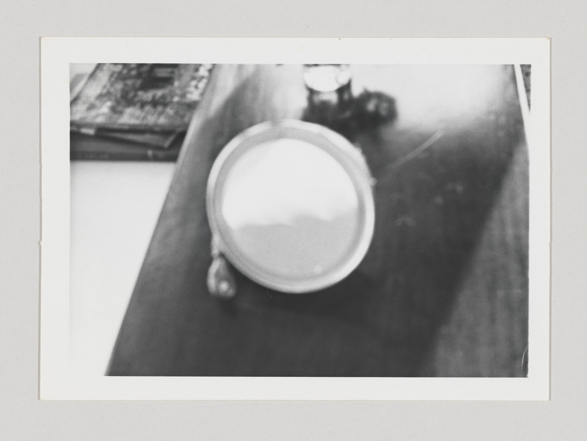A blurry round cup filled with liquid sits on a wooden table near stacked books.
