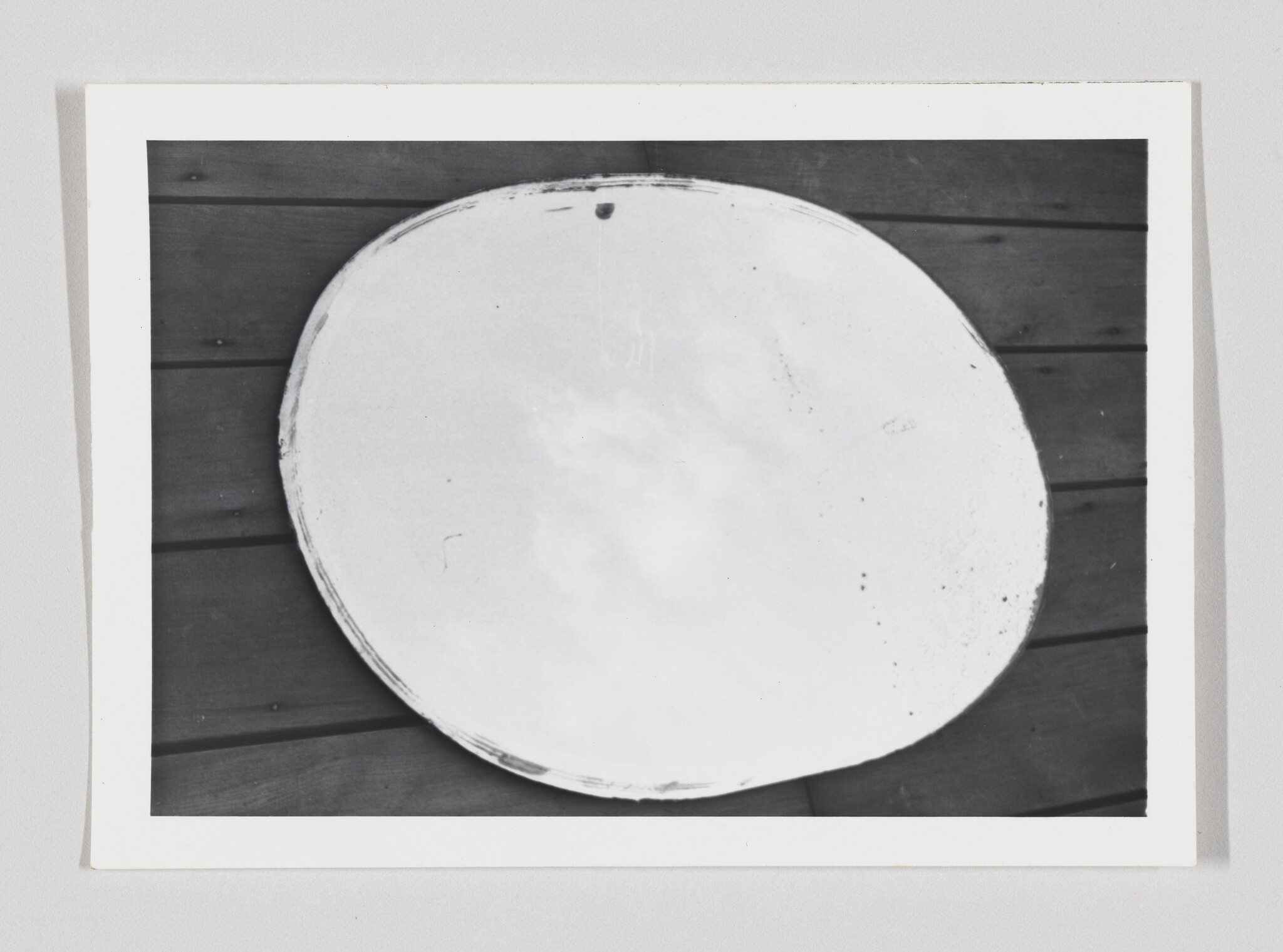 A large round white plate with worn edges resting on dark wooden floorboards.