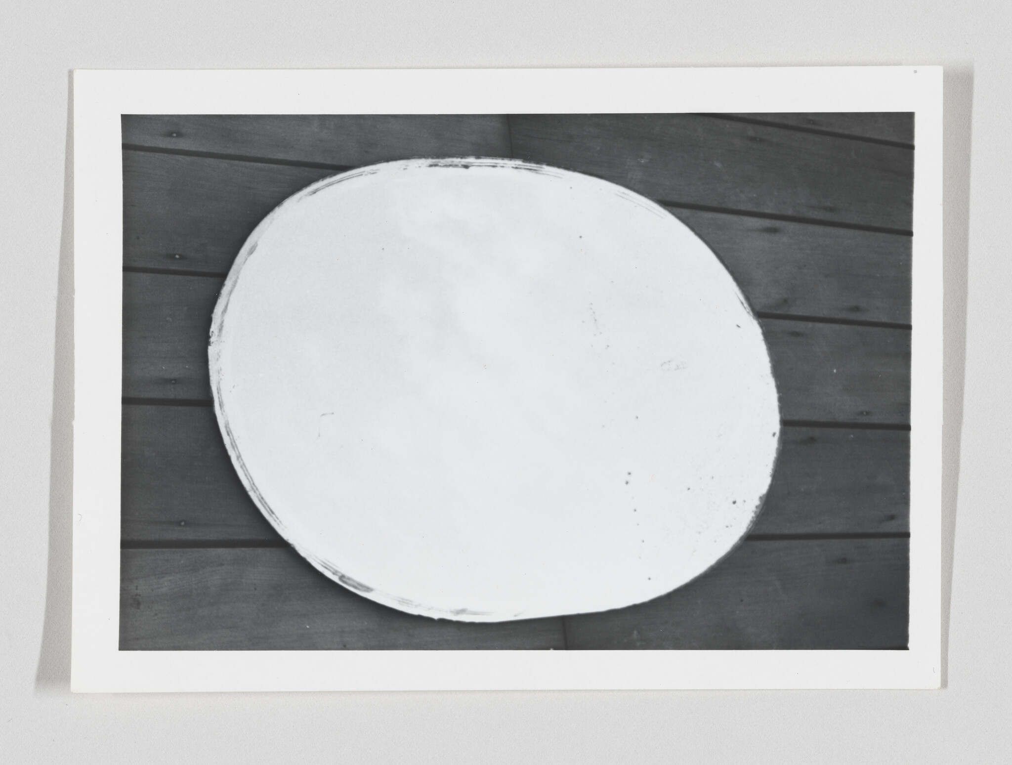 Large white circular panel resting on dark wooden planks with visible horizontal seams.