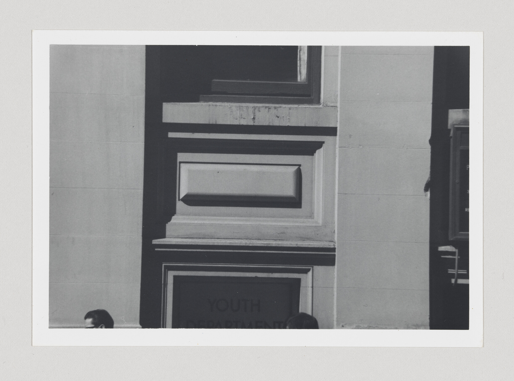 Stone building facade with layered decorative panels above an entrance labeled Youth Department, two heads visible.