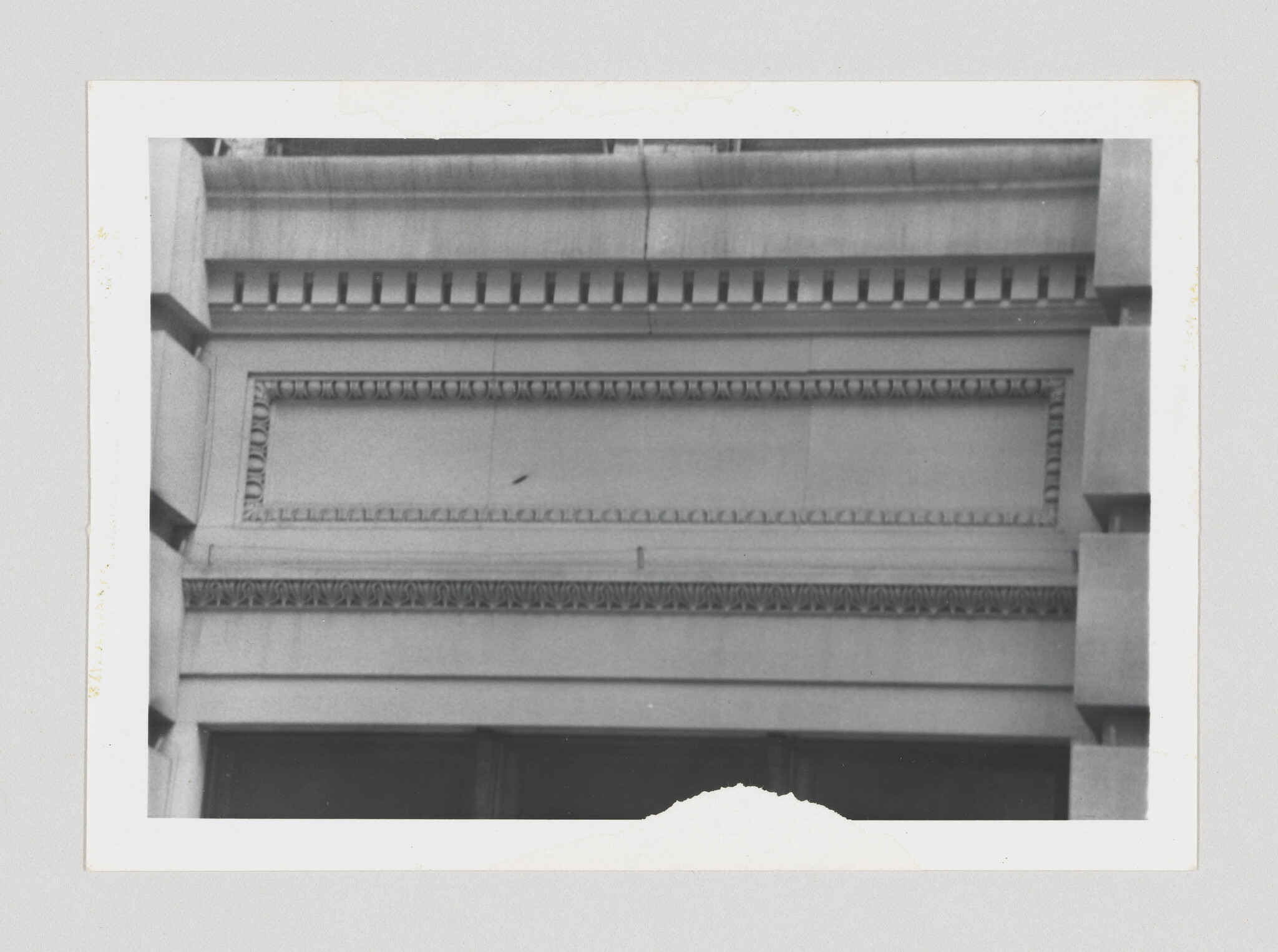 Stone building facade with decorative molding, dentil cornice, and rectangular recessed panel.