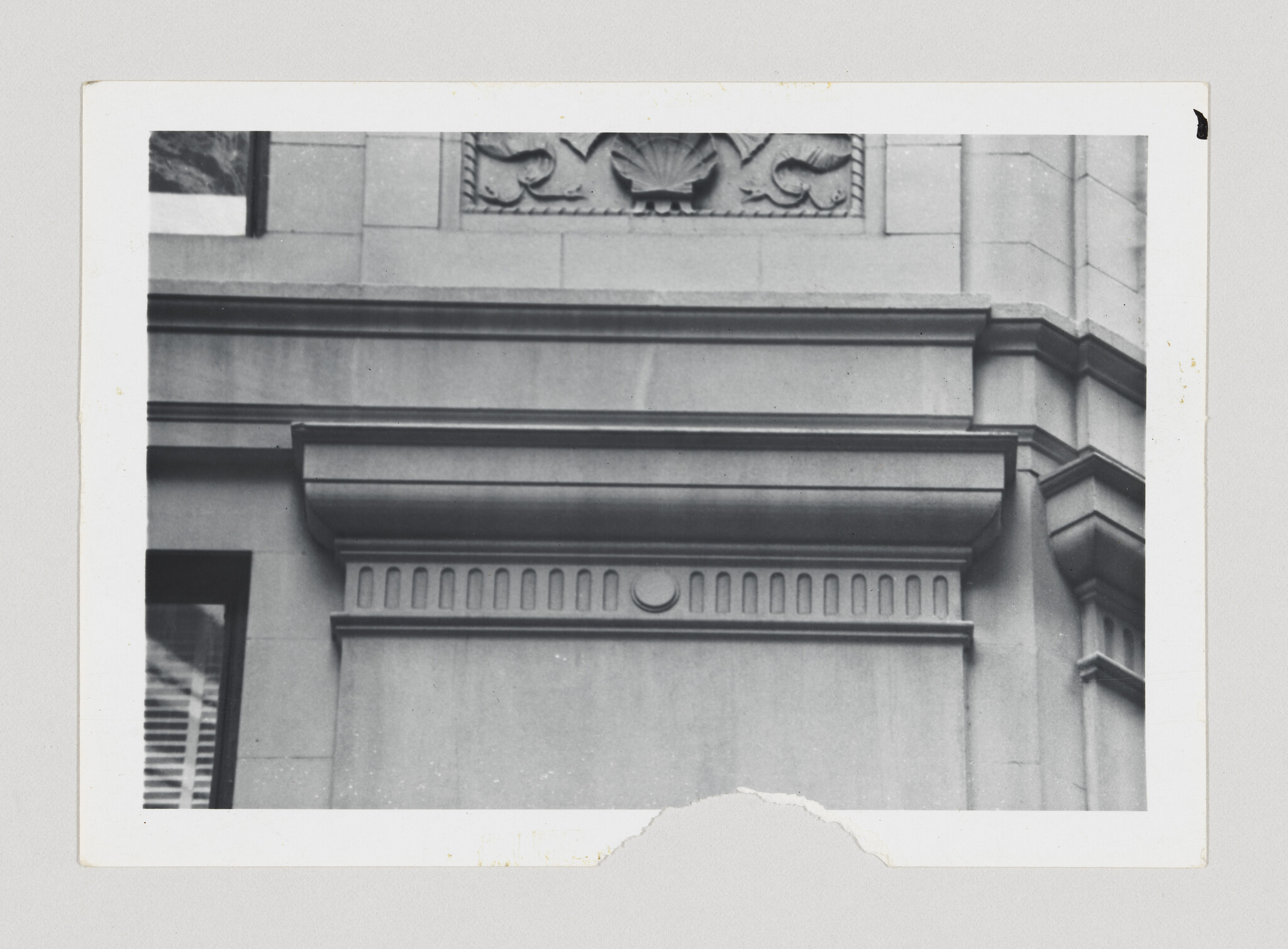 Stone building facade showing a decorative cornice and patterned frieze with rounded medallion.