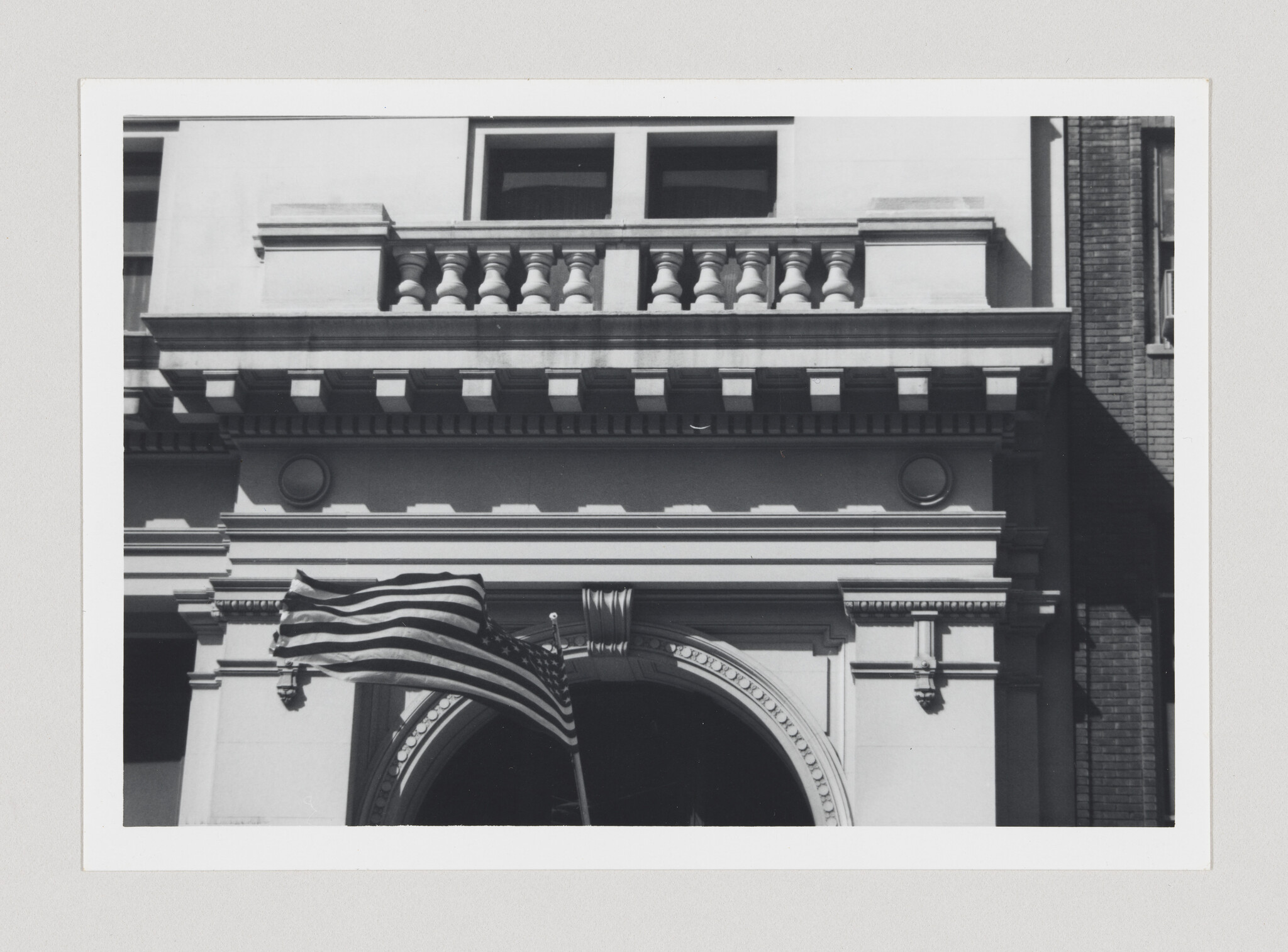 An American flag waves in front of a classical building entrance with decorative balcony.
