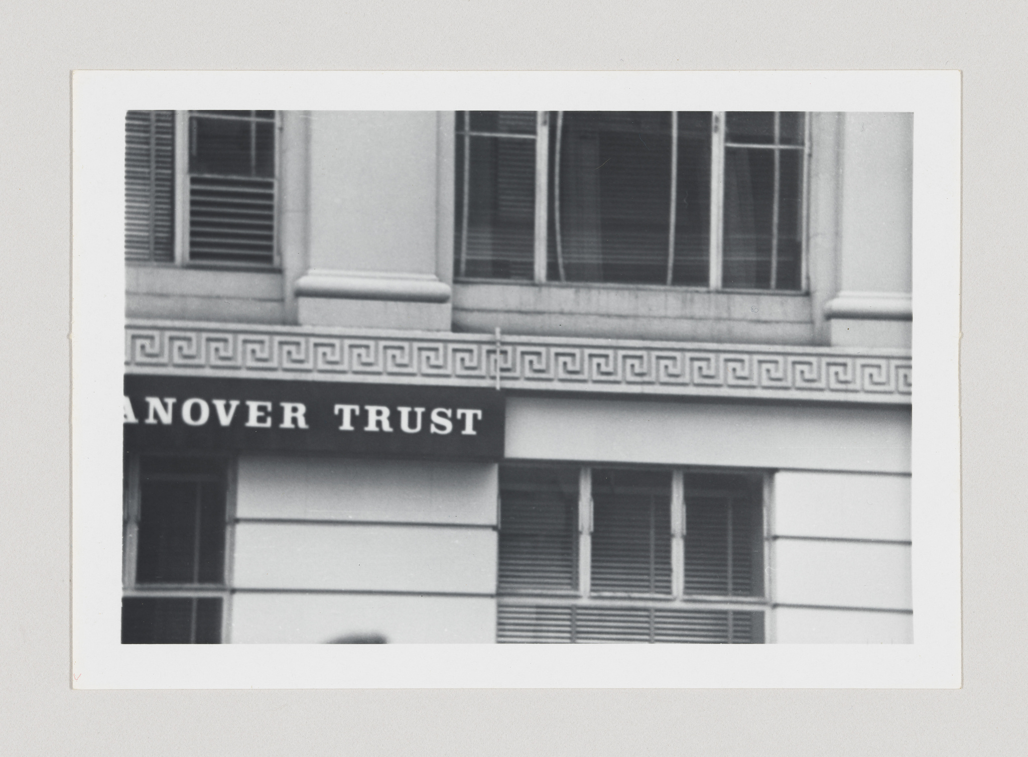 A black and white photograph of a building facade with the words "HANOVER TRUST" on a signboard, featuring architectural details like a Greek key pattern below the windows.