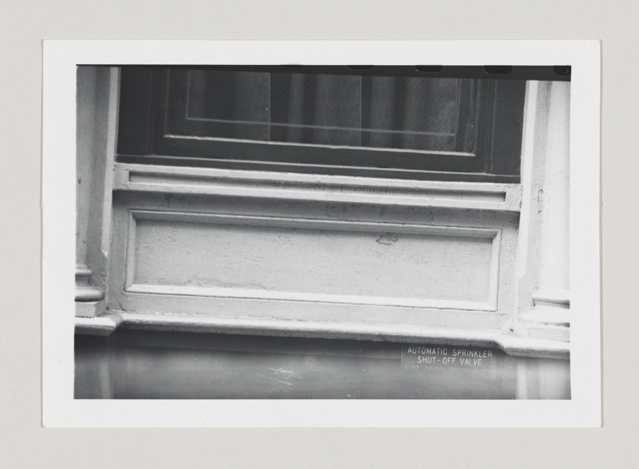 A building window with decorative paneling above a pipe labeled automatic sprinkler shut-off valve.