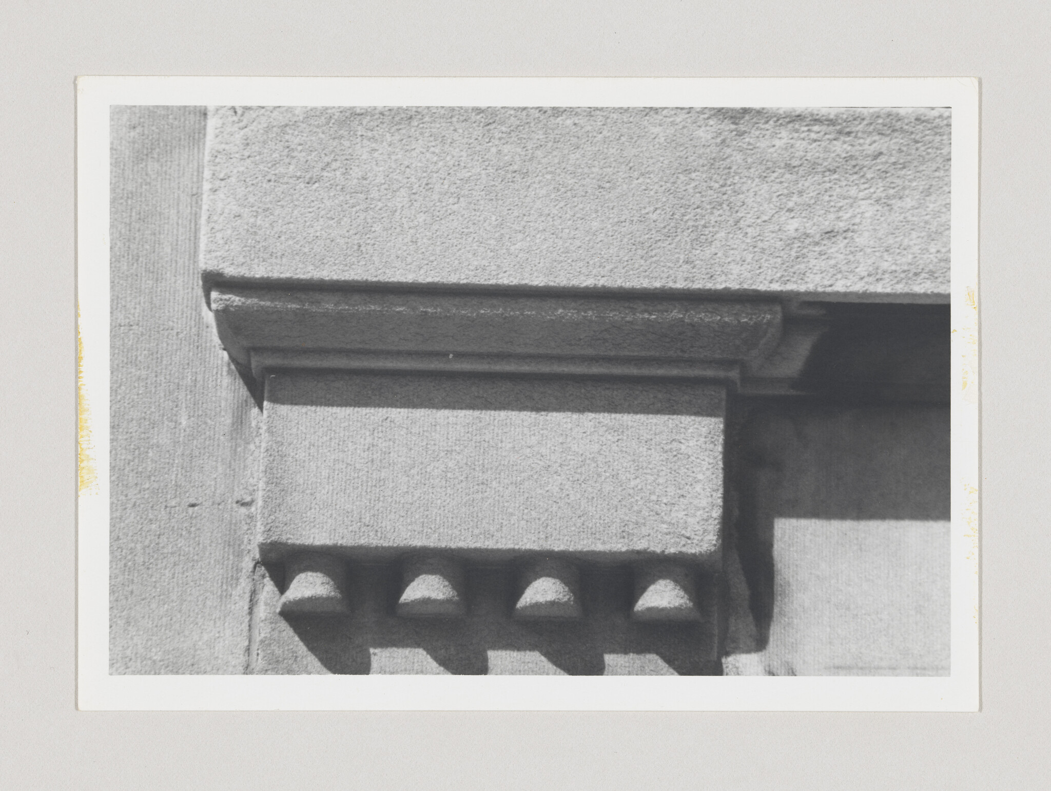 Close-up of a stone cornice showing five rounded dentils and sharp shadowed edges.