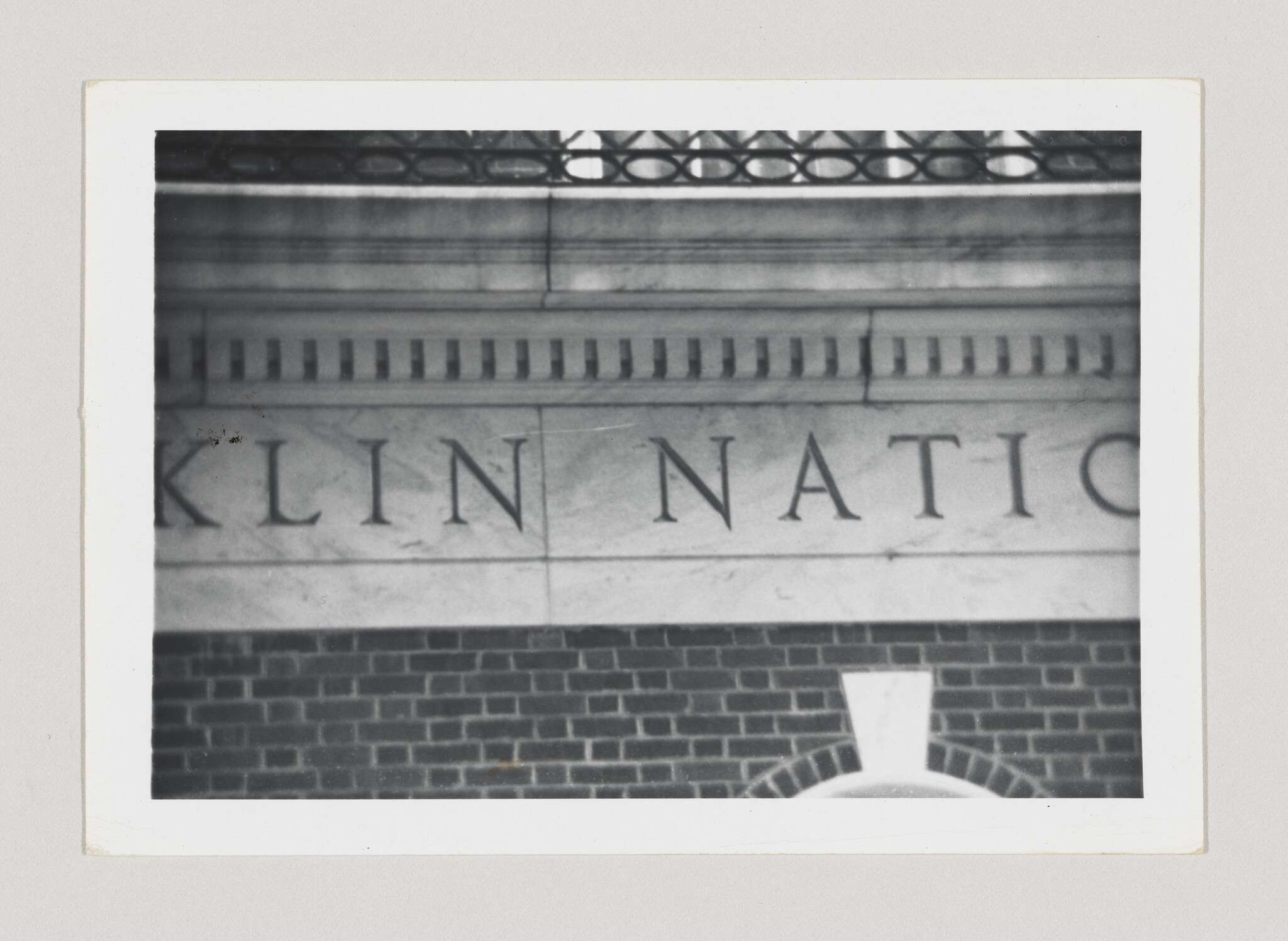 Stone building facade shows large carved letters above a brick wall and arched window.