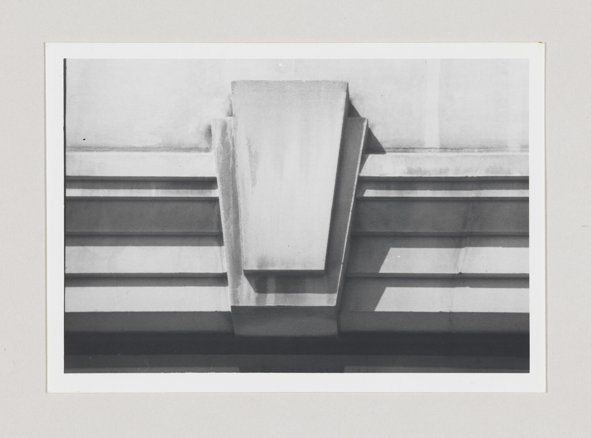 Concrete architectural cornice with stepped horizontal bands and a central tapered bracket casting shadows.