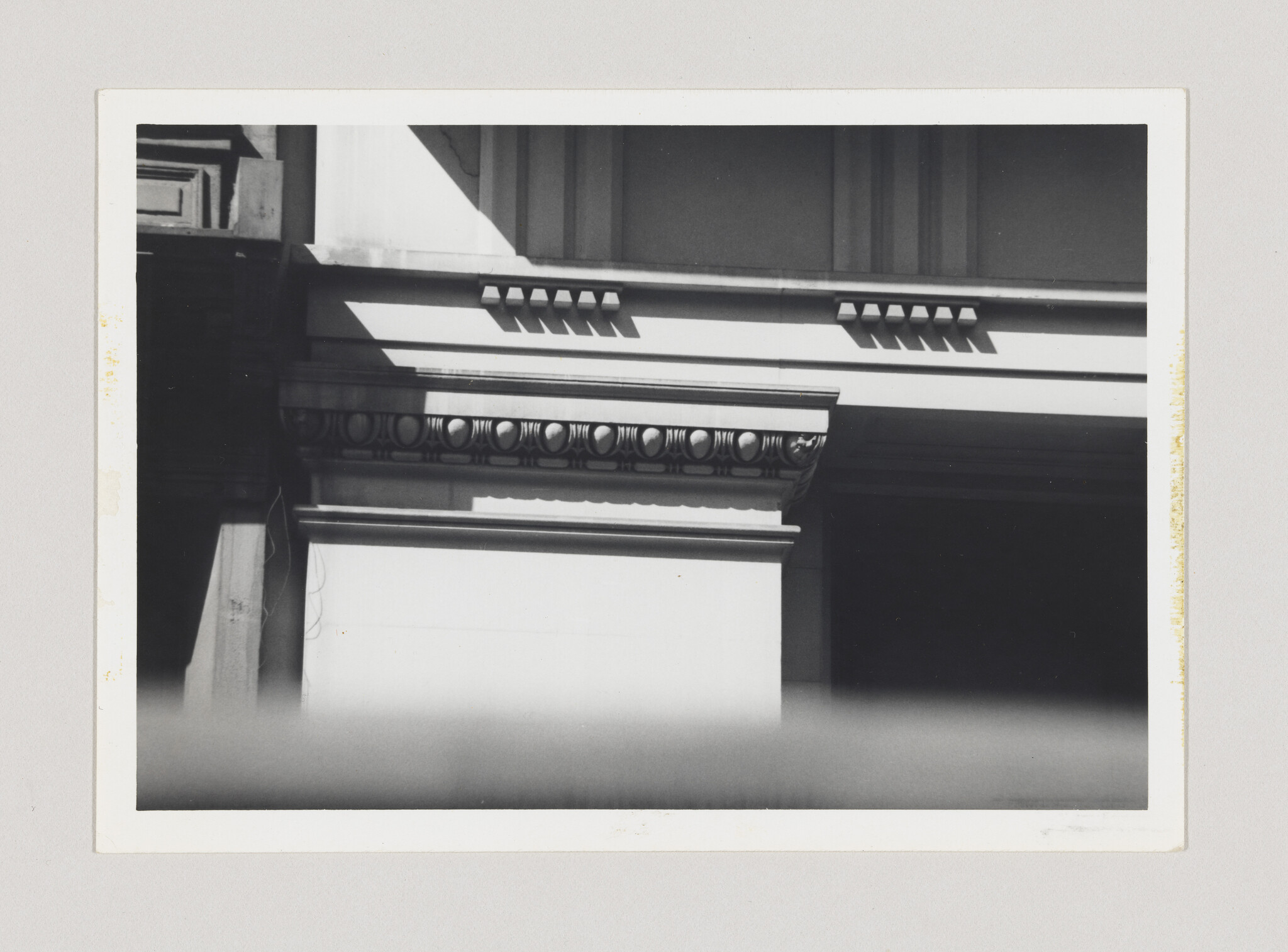 A black-and-white close-up of a classical building's entablature showing egg-and-dart molding and dentils.