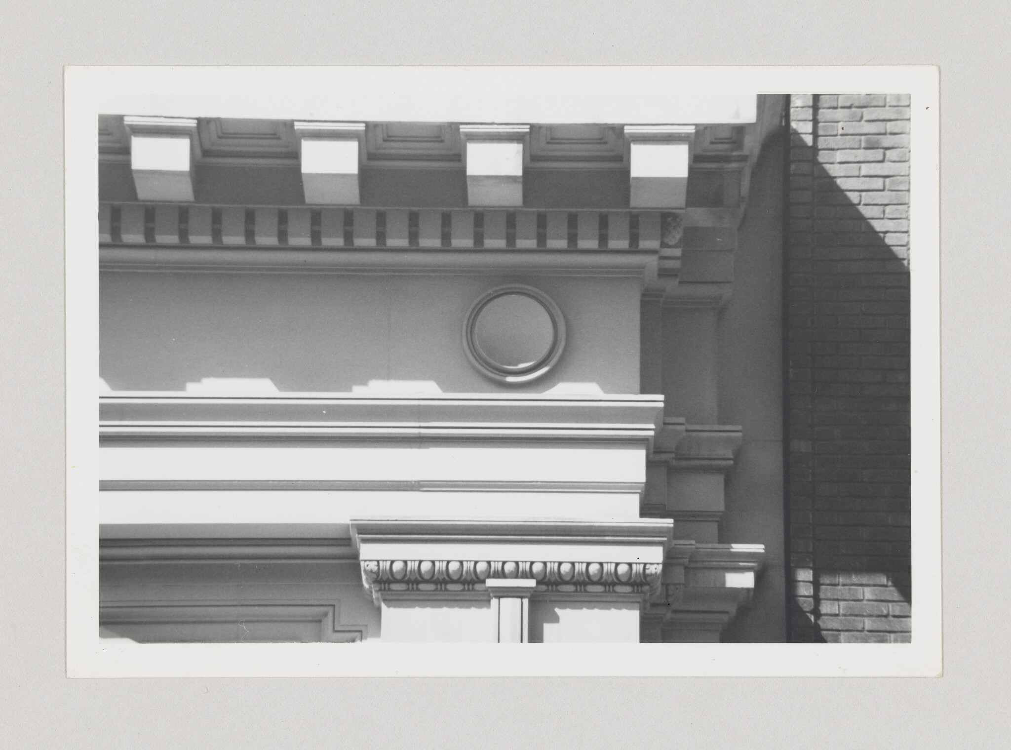 Classical building facade with decorative cornice, round medallion, and adjacent brick shadow.