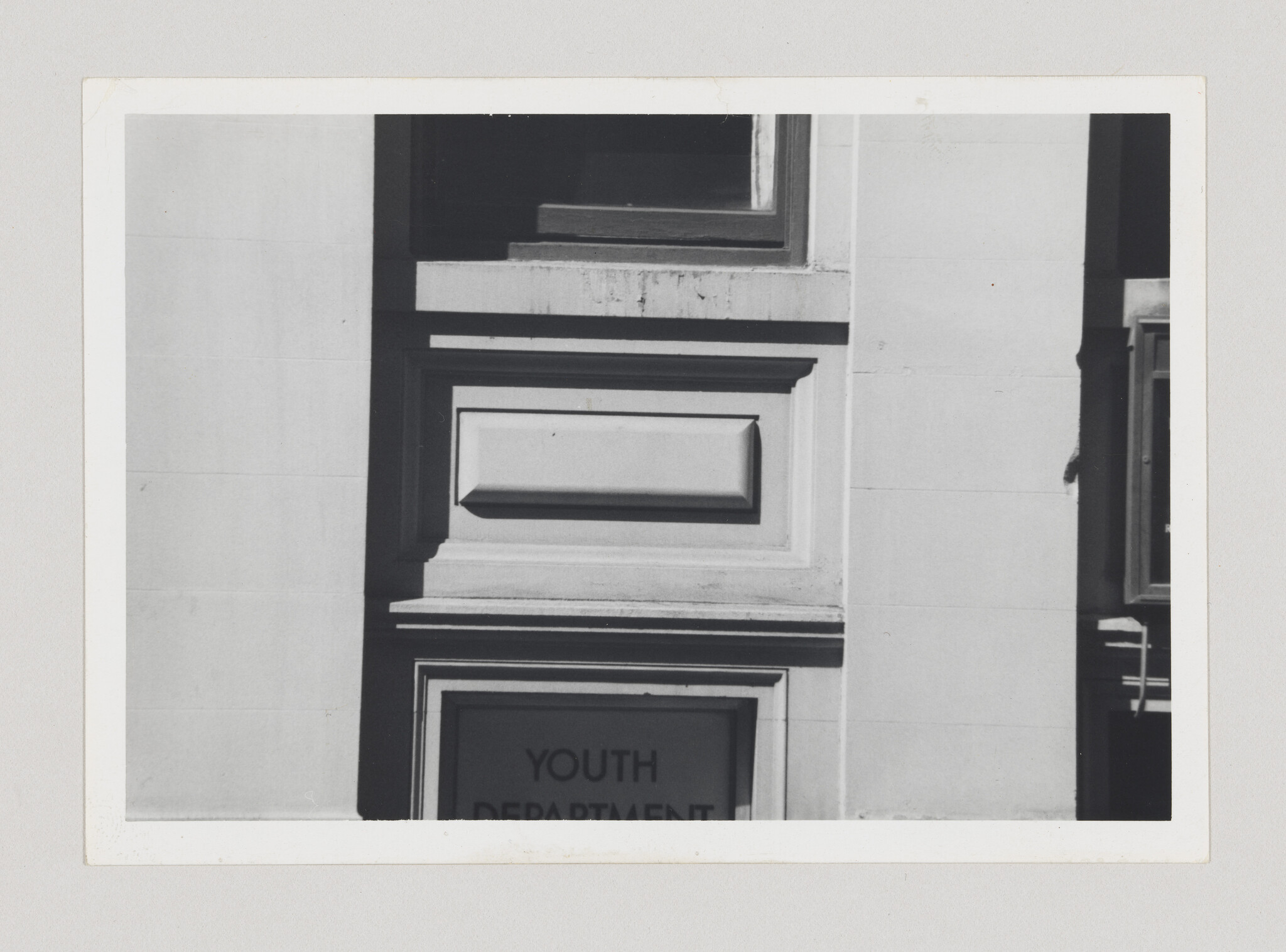 Stone building facade with rectangular decorative panels and a partially visible sign reading youth department.