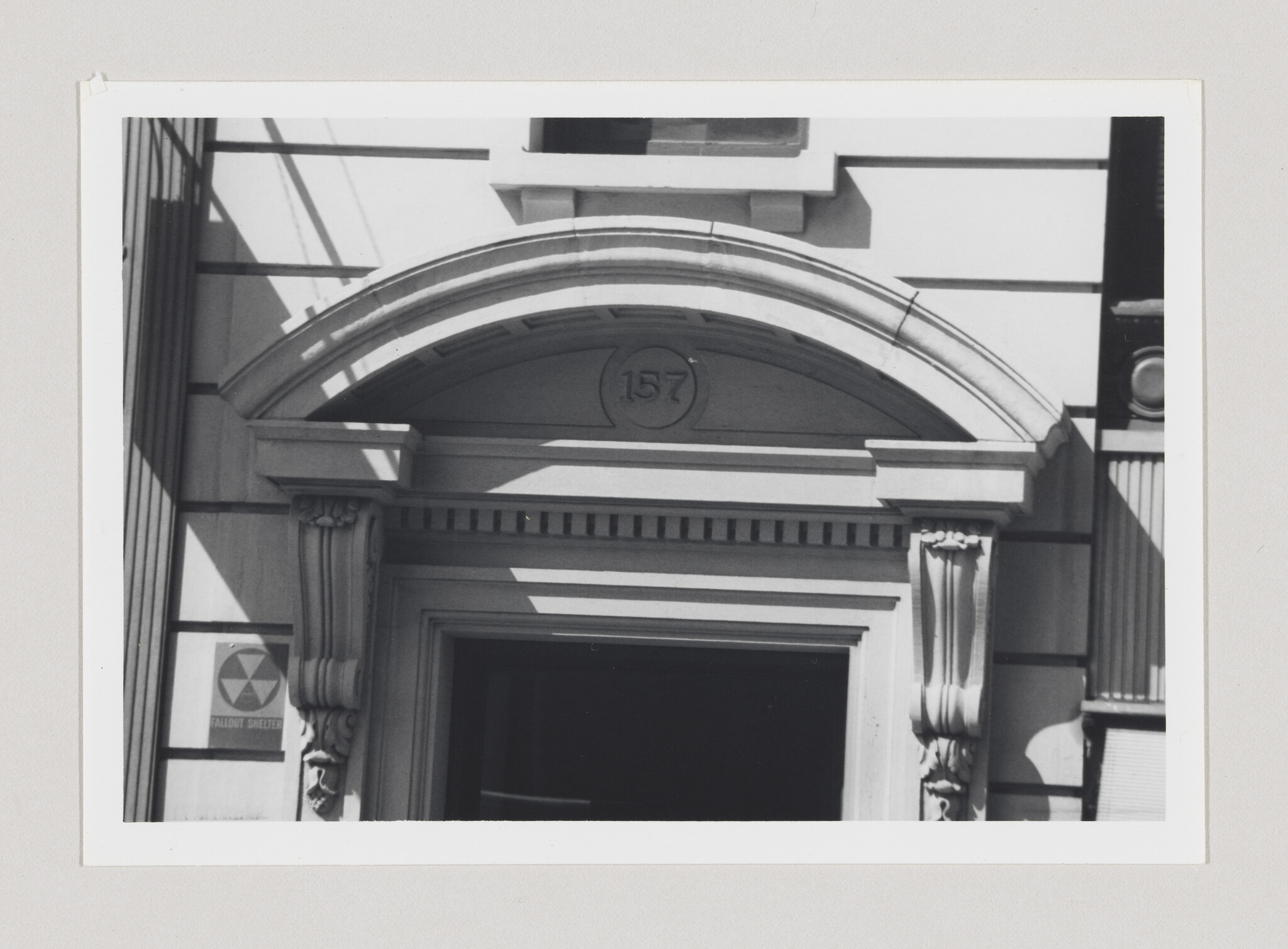 Stone building entrance with decorative arch labeled 157 and a small fallout shelter sign.