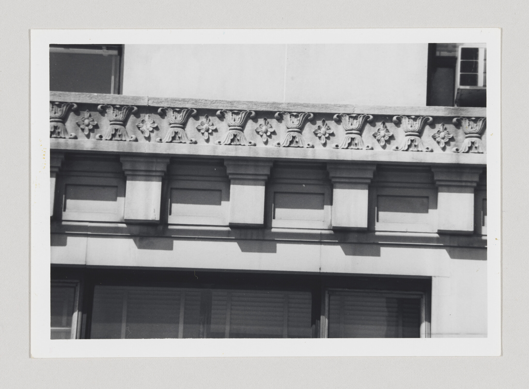Ornate stone building facade with carved floral motifs above rectangular window openings and cornice.