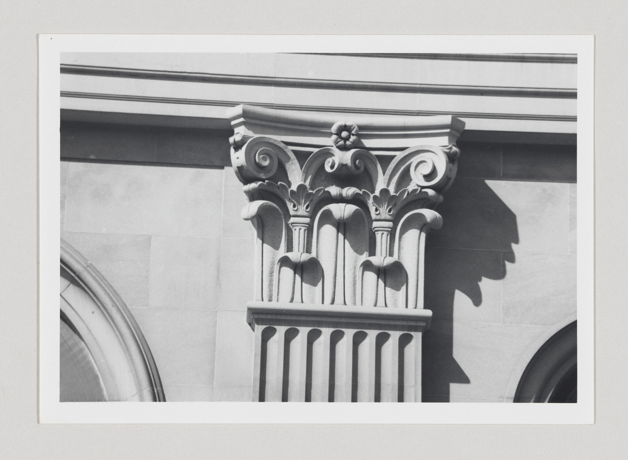 Ornate carved column capital with acanthus leaves and scrolls casting a shadow on the wall.
