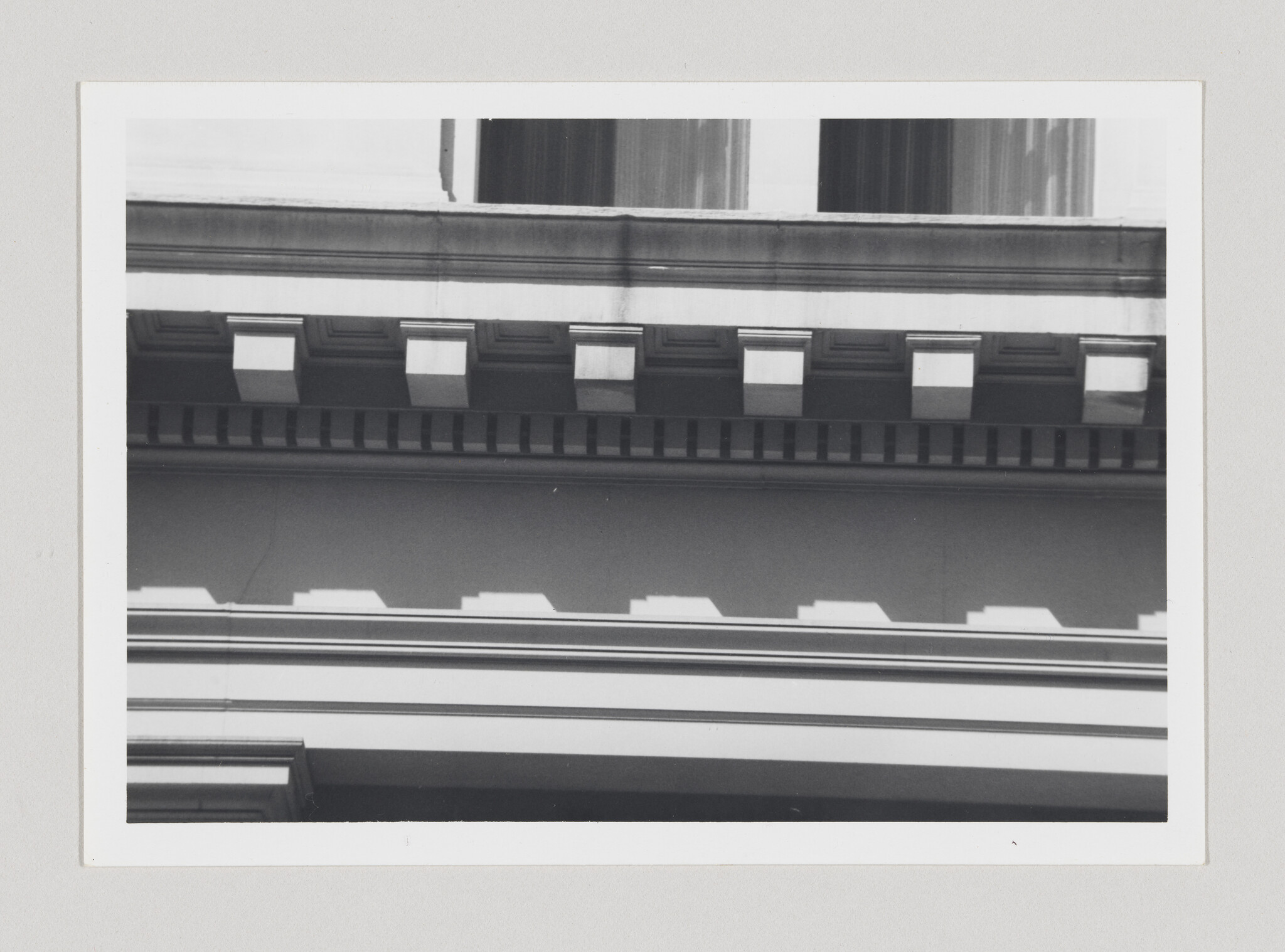 A row of rectangular dentils on a building cornice casting repeating shadows across the facade.