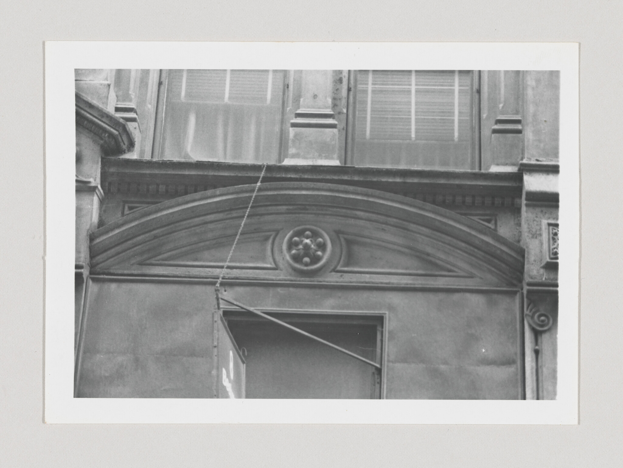 Stone arched pediment with central rosette above a partially open doorway and hanging chain.
