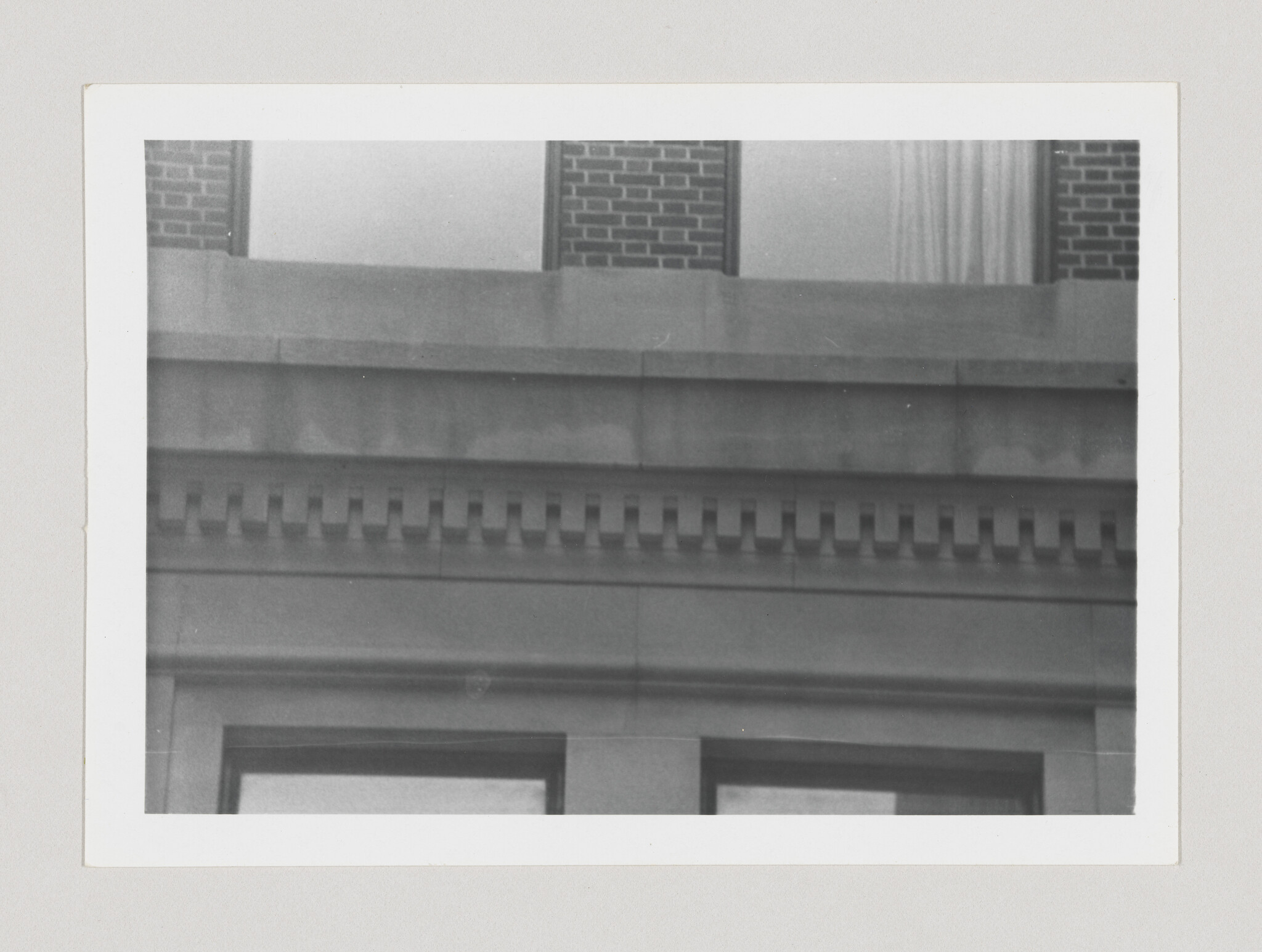 Close-up of a building facade showing decorative dentil molding above two windows.