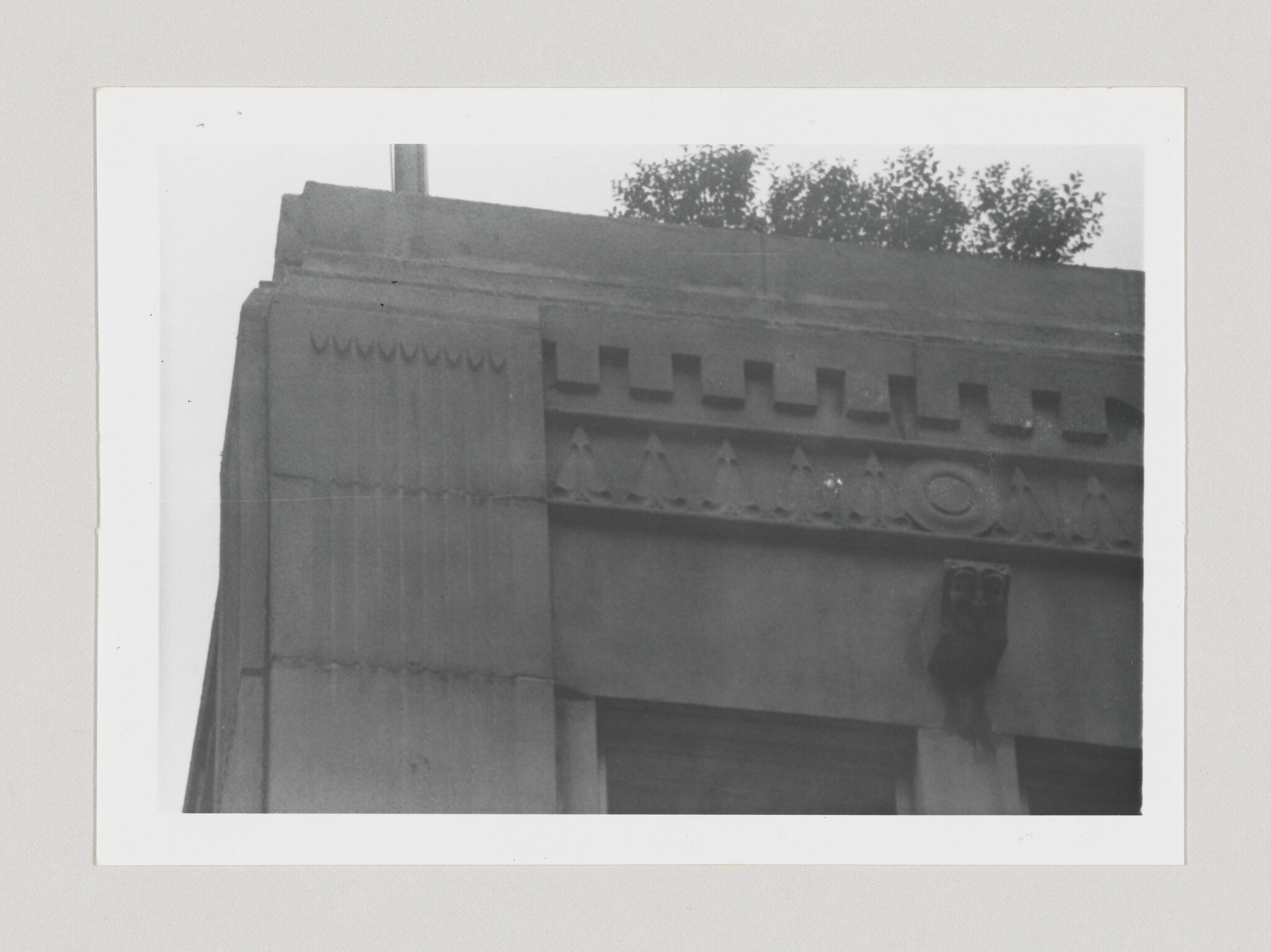 Stone building facade with decorative cornice, triangular patterns, and a small ornamental gargoyle.