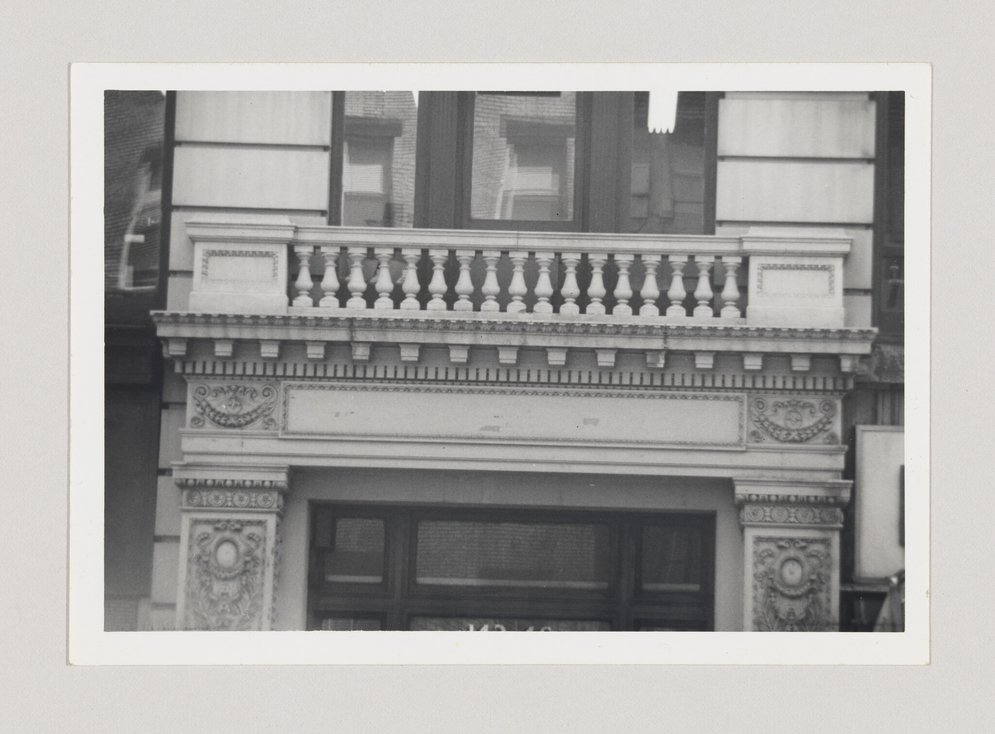 Ornate stone building facade with balustrade, dentil cornice, and decorated column capitals above an entrance.