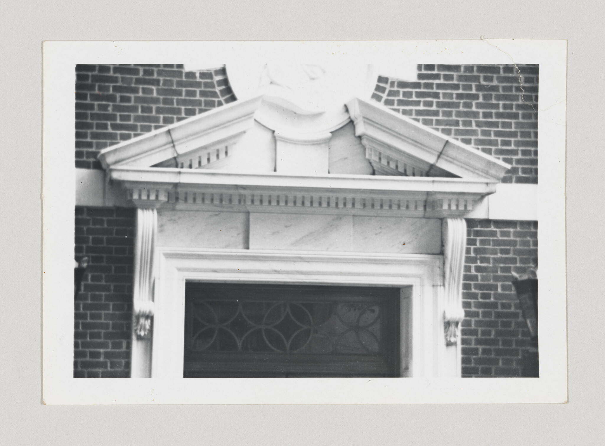 Classical stone pediment and columns above a brick building entrance with decorative window.