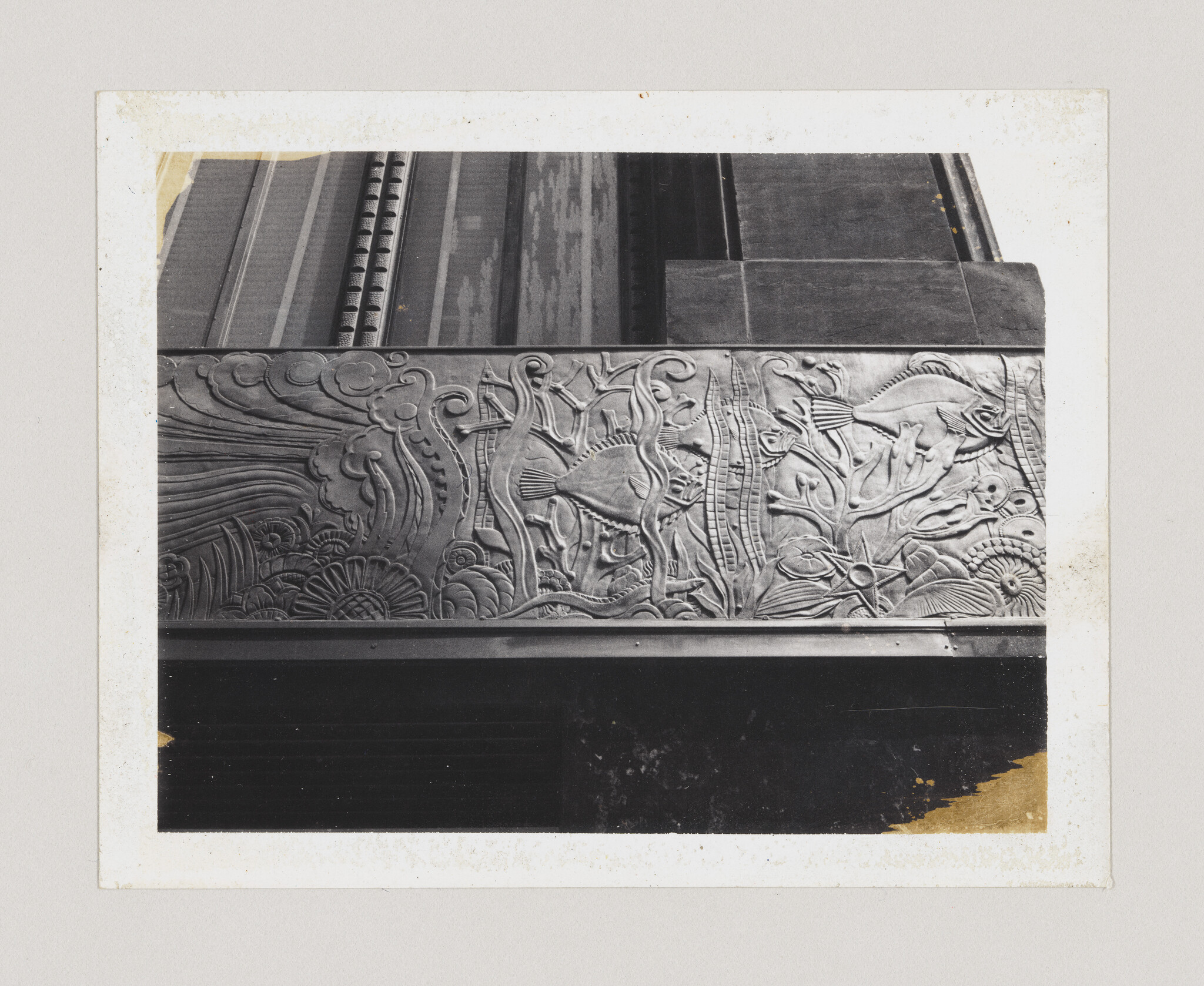 Ornate metal frieze showing fish swimming among seaweed, shells, and swirling water patterns.