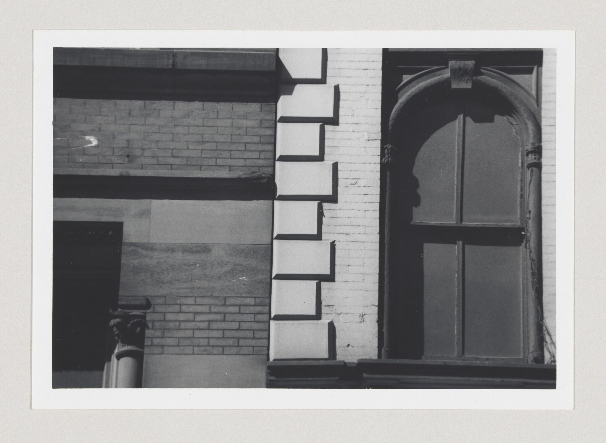 A building facade shows an arched closed window, geometric stone blocks, and a decorative column capital.