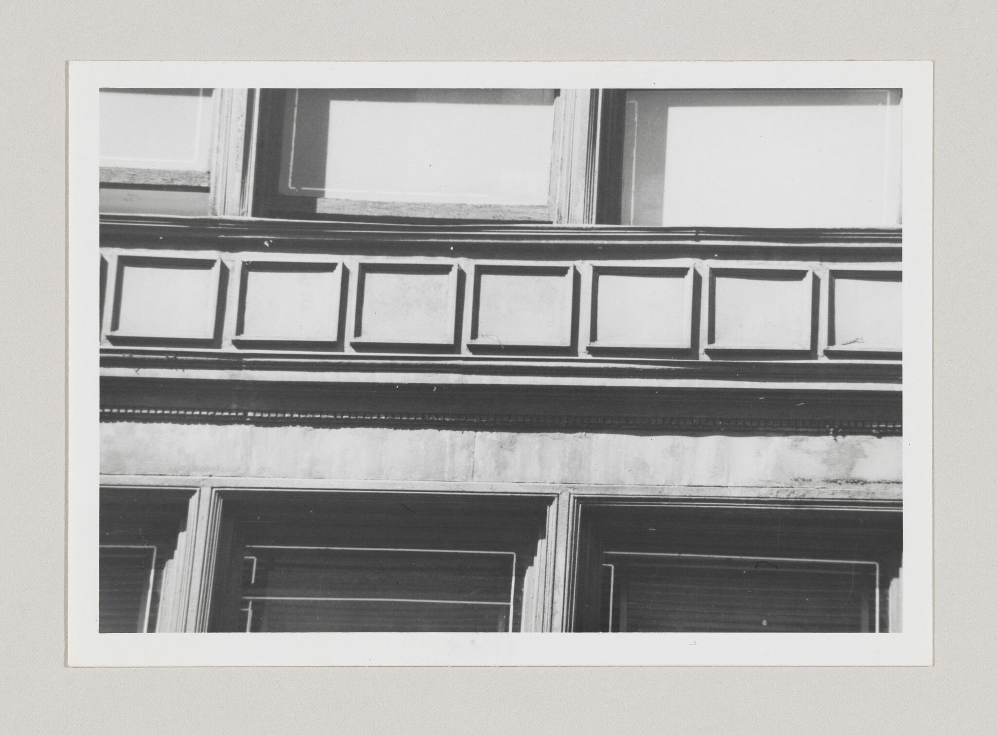 A building facade with a row of rectangular recessed panels above large first-floor windows.