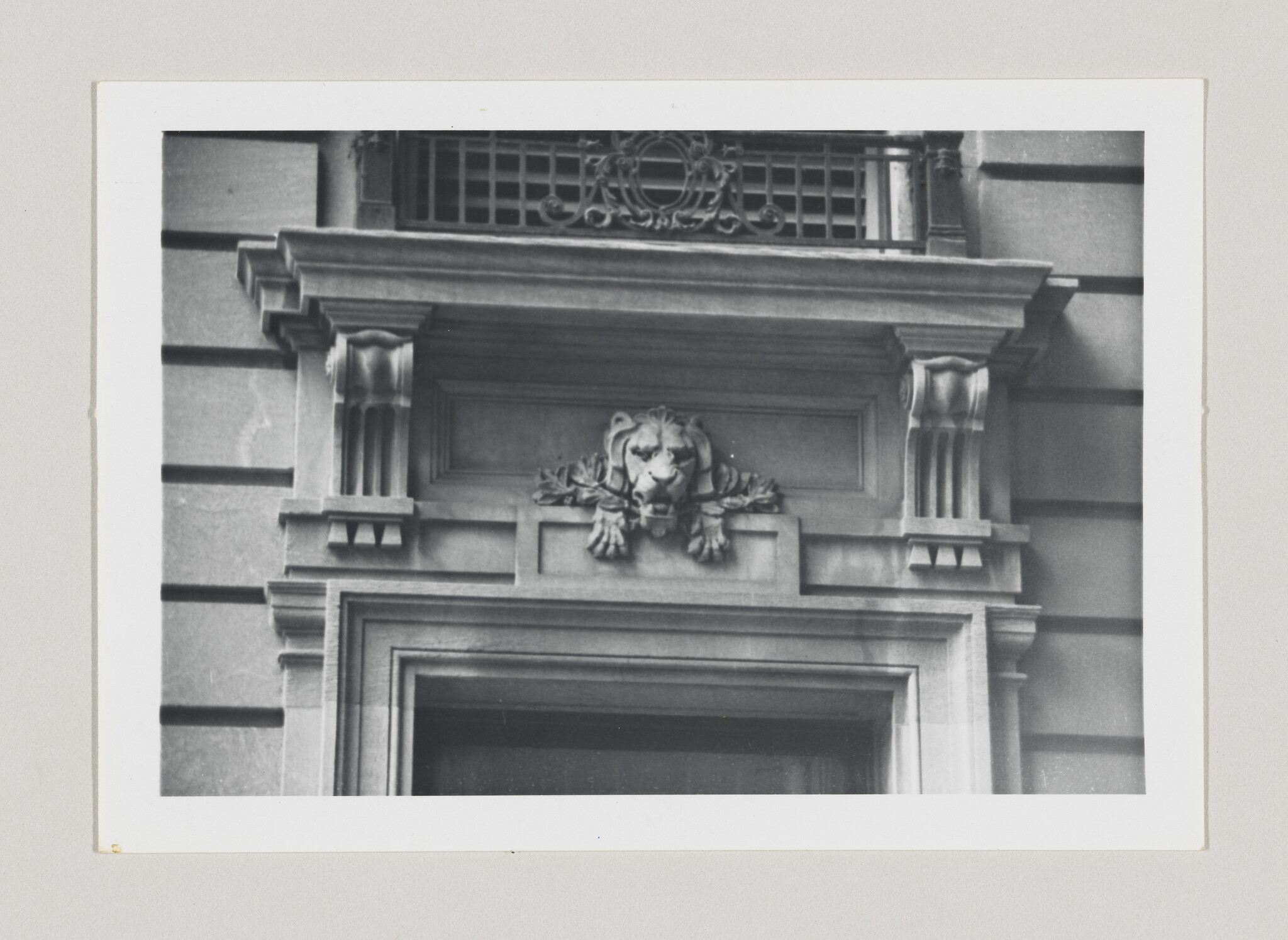 Stone lion head ornament above an ornate building doorway with decorative columns and molding.