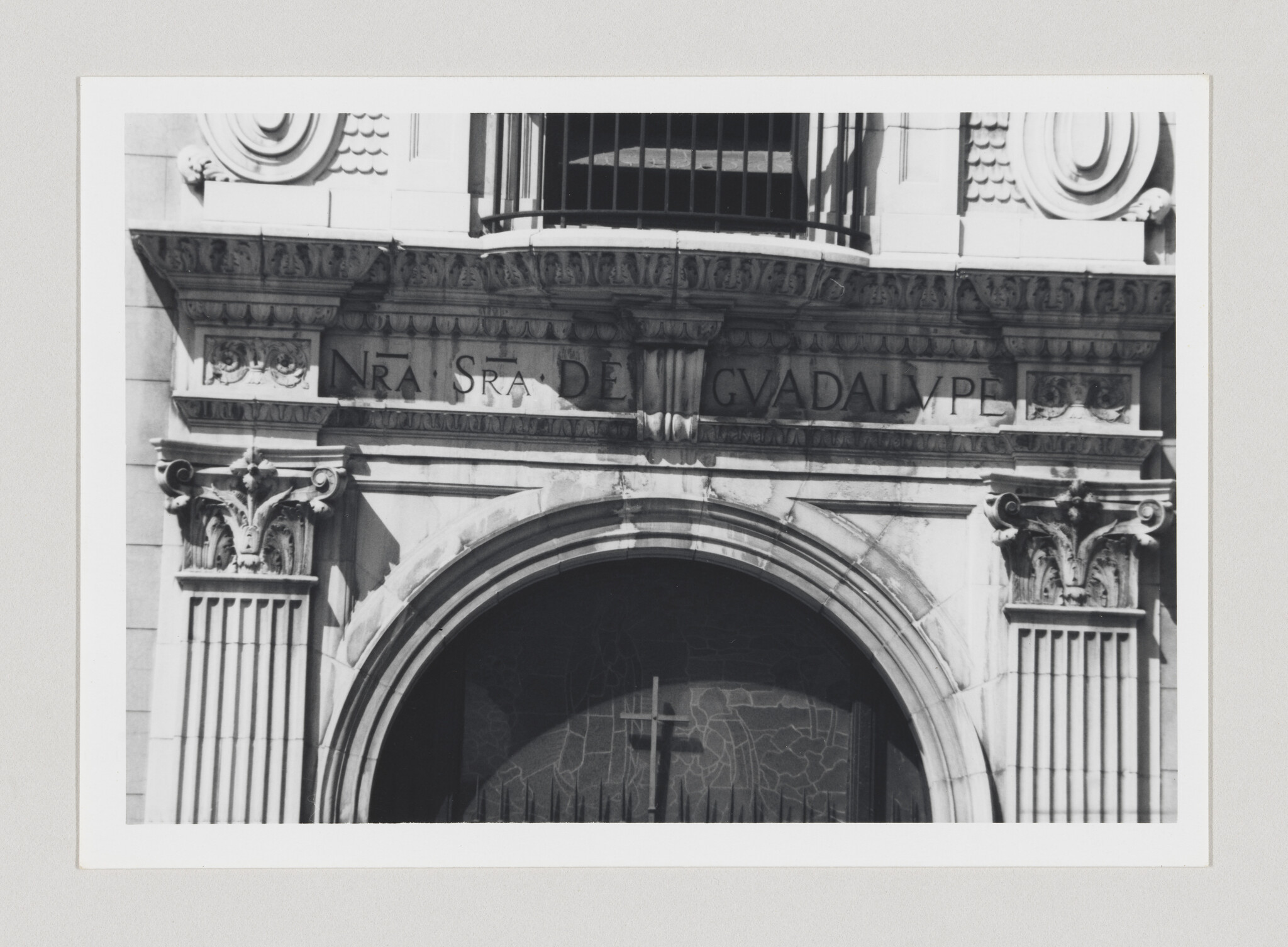 Stone arched church entrance with carved columns, inscription "NRA SRA DE GUADALUPE" and a cross.