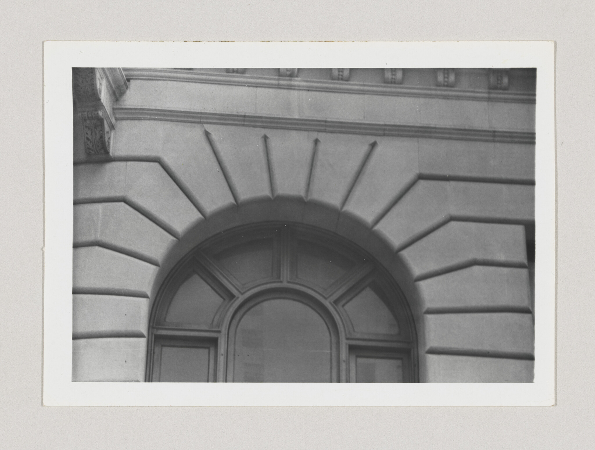 Arched stone doorway with fanlight window and radiating block patterns on a classical building.