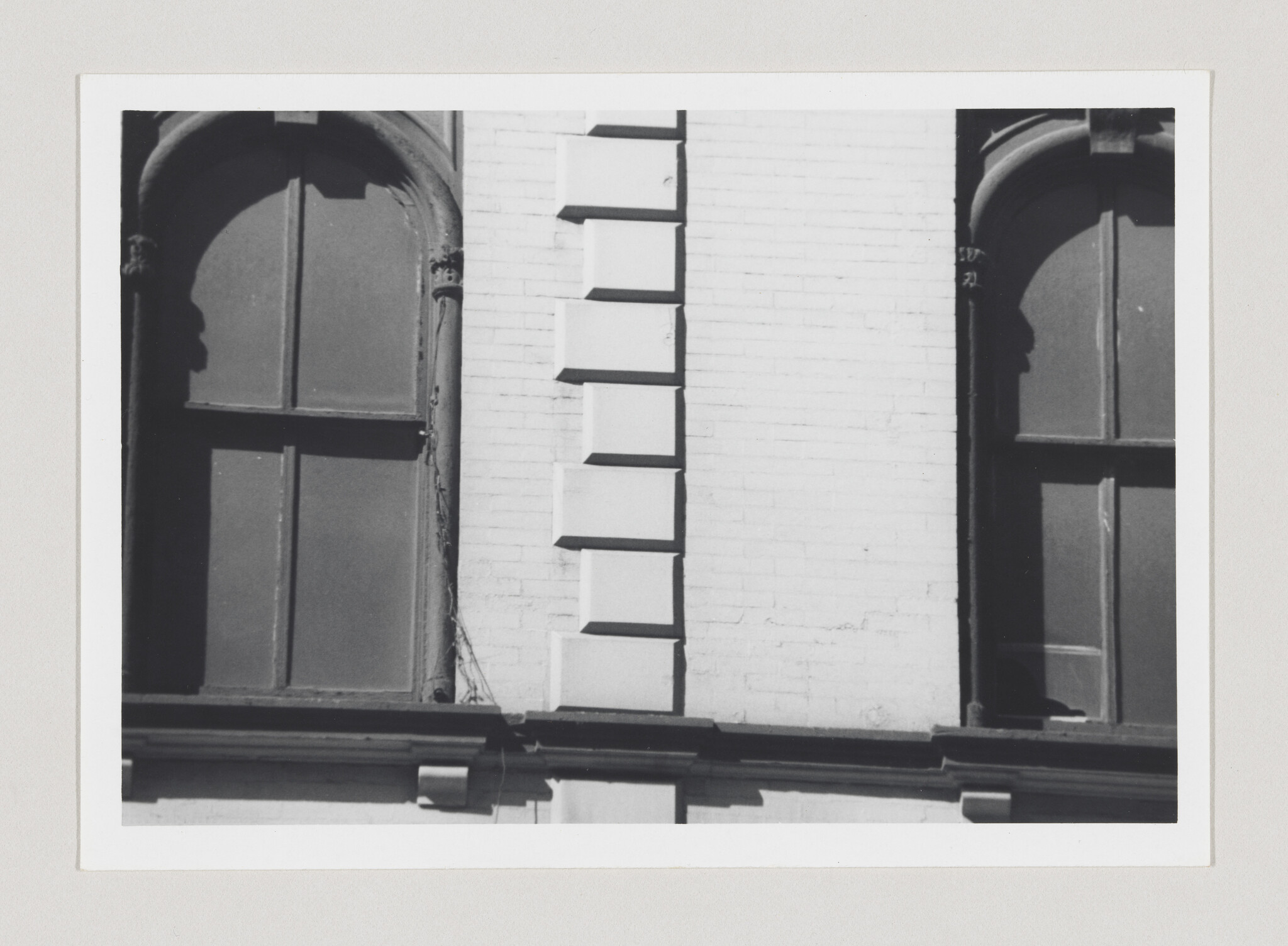 Two tall arched windows flanking a narrow brick section with decorative rectangular quoins.