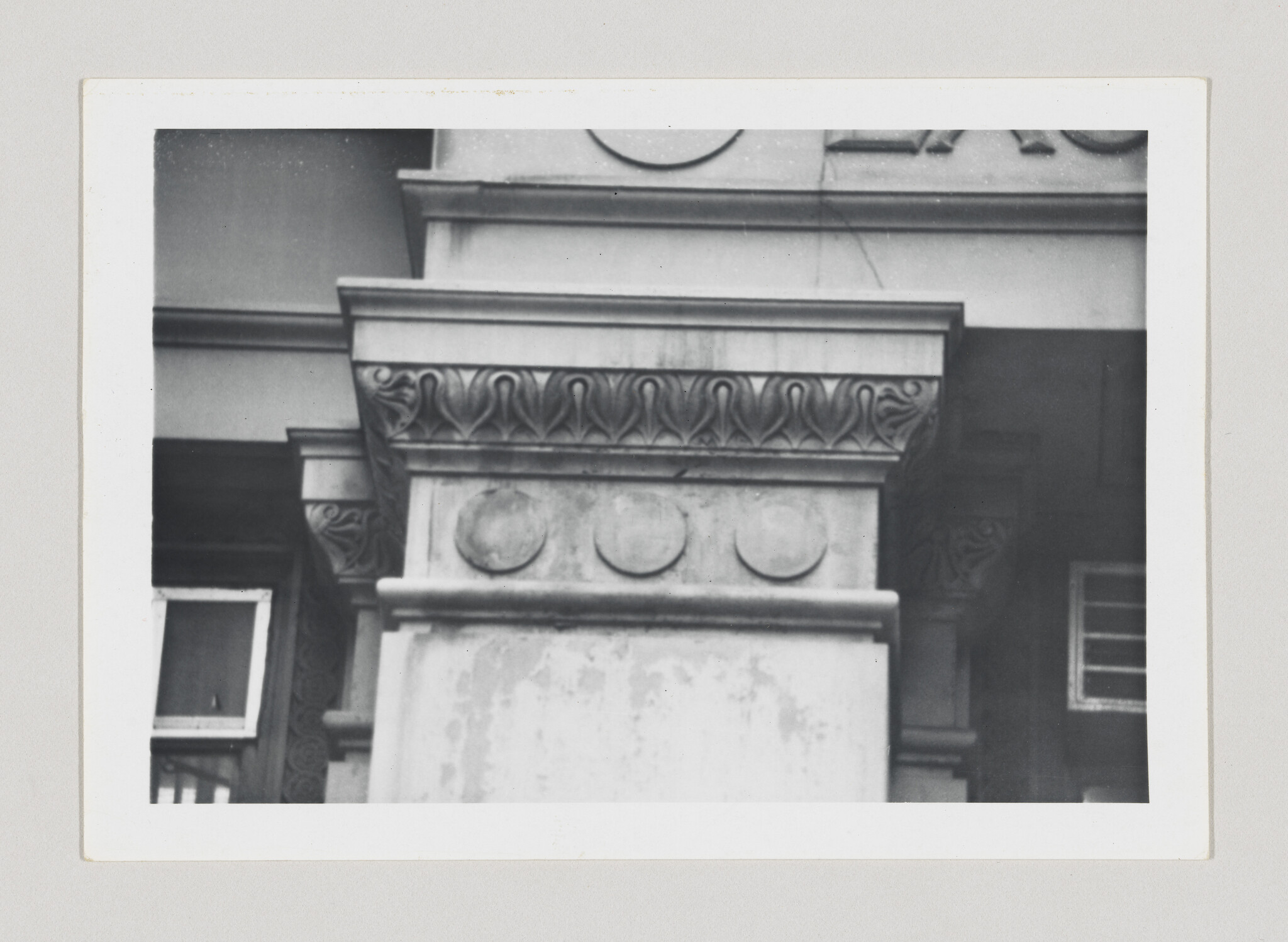 Stone column capital with carved leaf motifs and three round medallions on building facade.