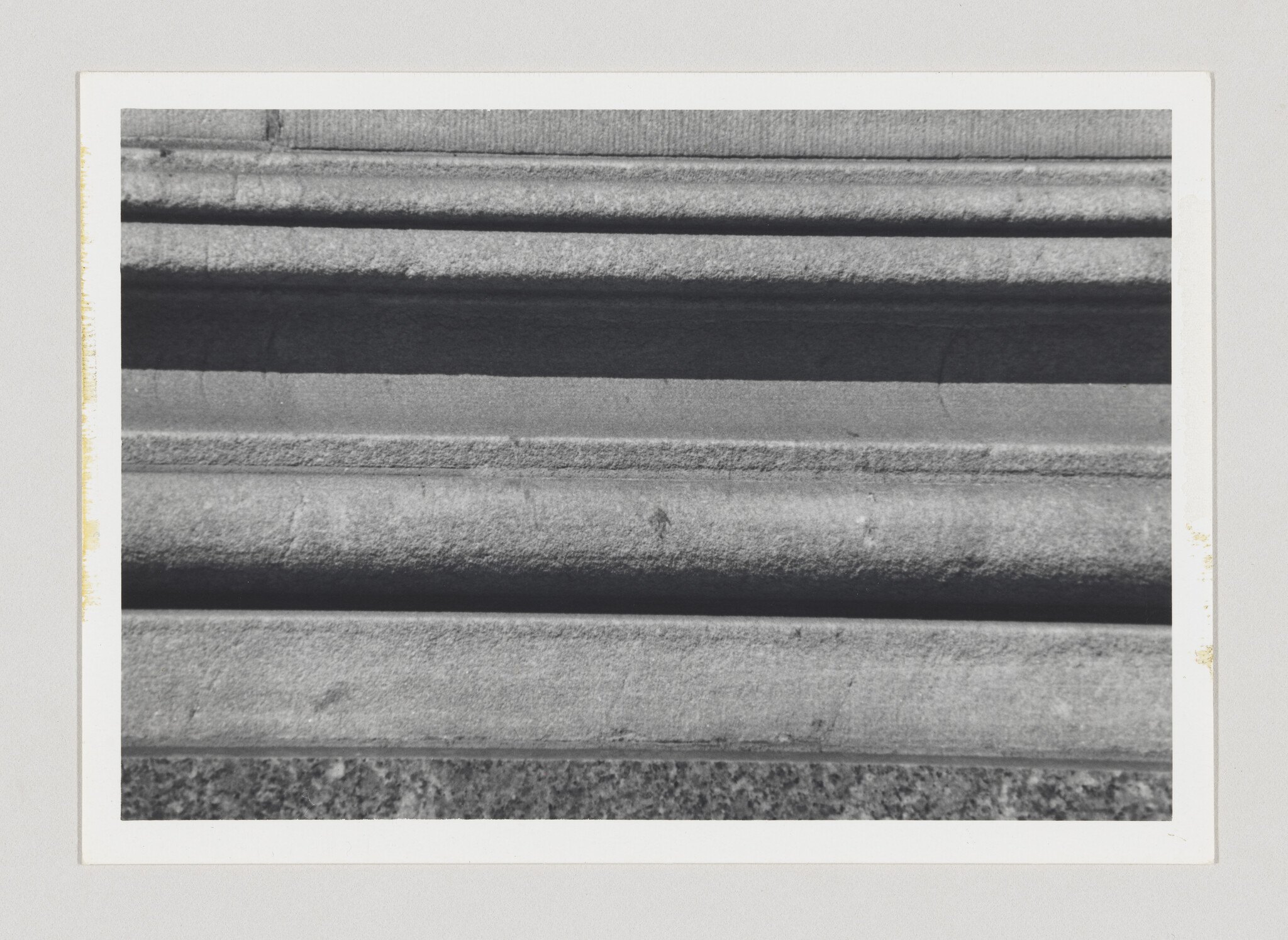 Horizontal stone molding shows layered grooves and rough texture near a building base.