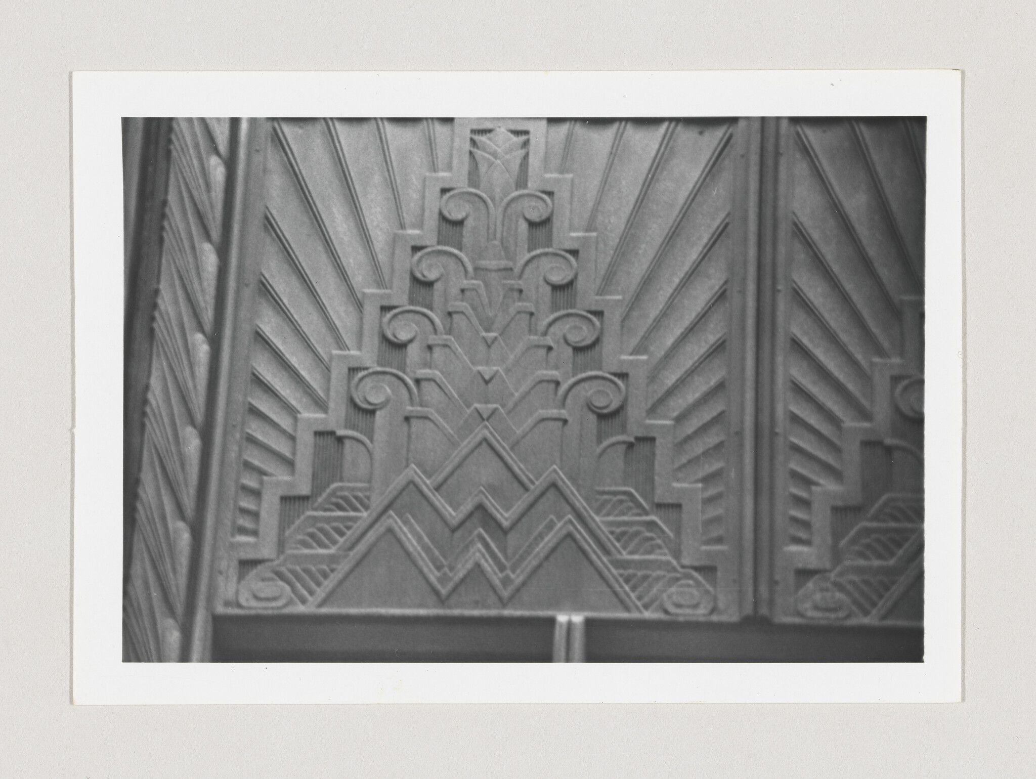 Carved Art Deco wooden panel with stepped geometric patterns, radiating lines, spirals, and zigzag motifs.