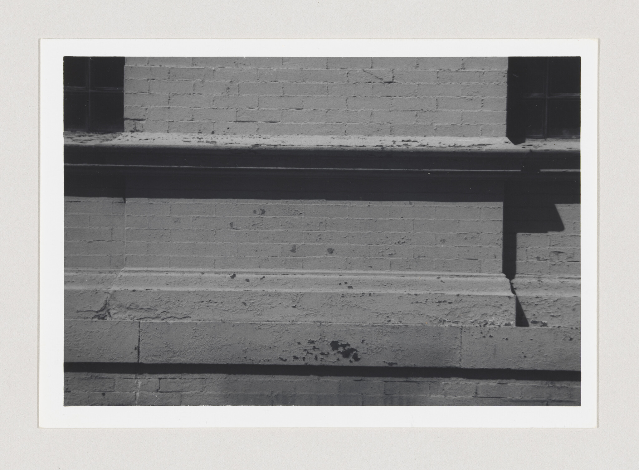 Brick wall with layered horizontal ledges and a rectangular shadow cast by a protruding pipe.