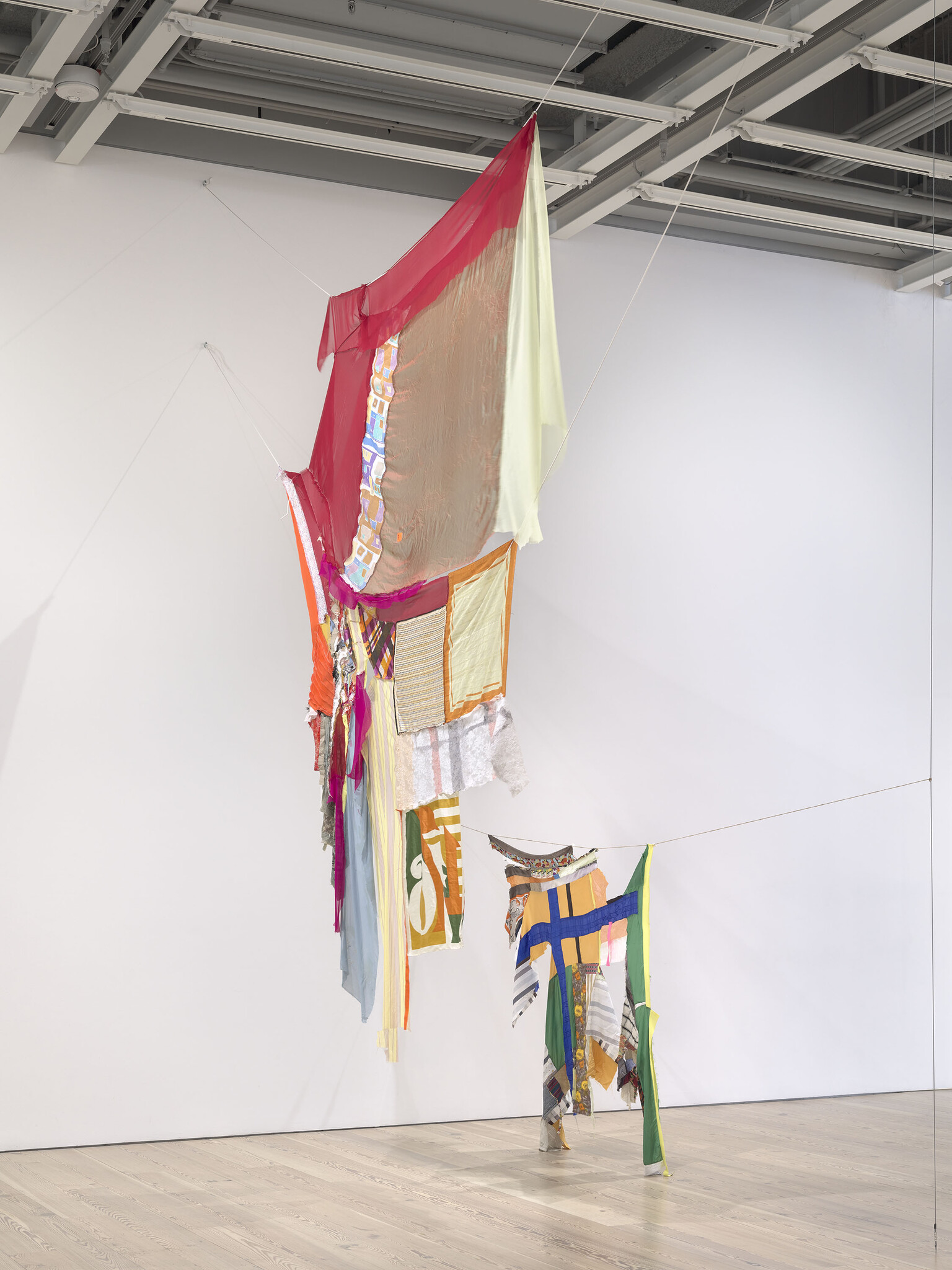 Colorful patchwork fabric panels suspended from the ceiling forming a tall hanging textile sculpture.