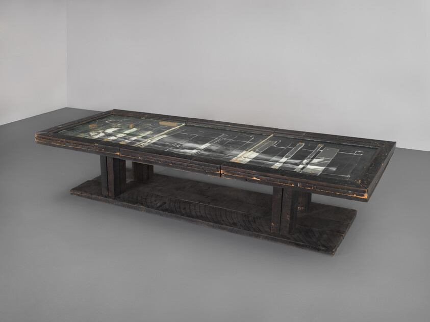 Long, dark wooden table with a glass top displaying abstract black and white images or patterns underneath.