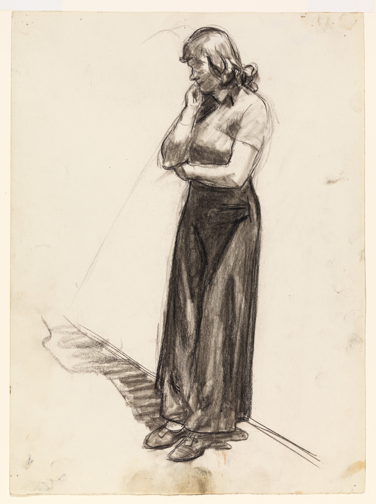A charcoal sketch on paper depicting a standing woman in profile view, with her left hand raised to her chin in a thoughtful pose. She wears a short-sleeved blouse and wide-legged trousers, with her hair tied back. The drawing is detailed with shading and contouring, capturing the folds of her clothing and the expression of contemplation on her face. The background is mostly blank, with only a few sketch lines.