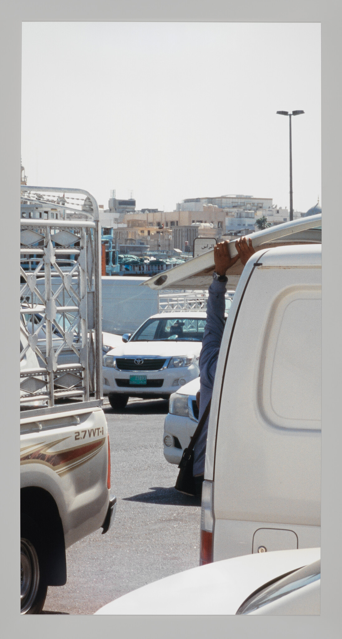 A person reaches up to close a white van's rear door in a busy parking area.
