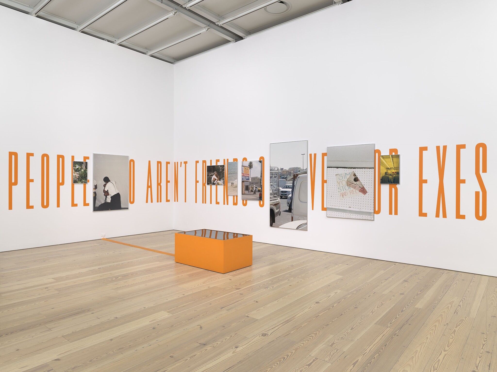 Gallery wall with large orange lettering, mounted photos, mirrors, and a low orange bench.