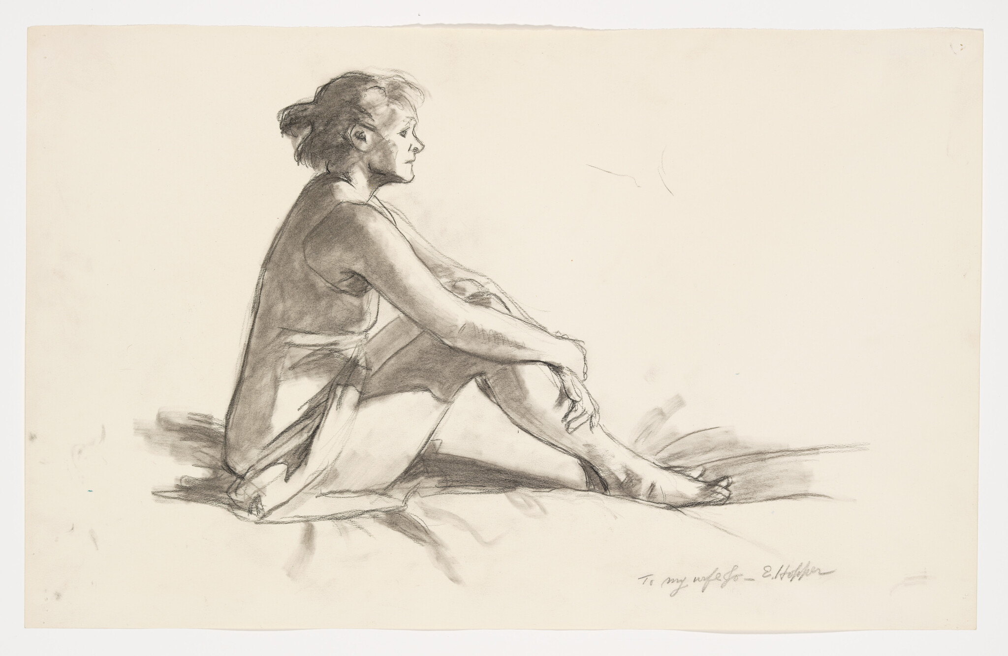 A woman sits in profile with her arms wrapped around her knees, looking forward.