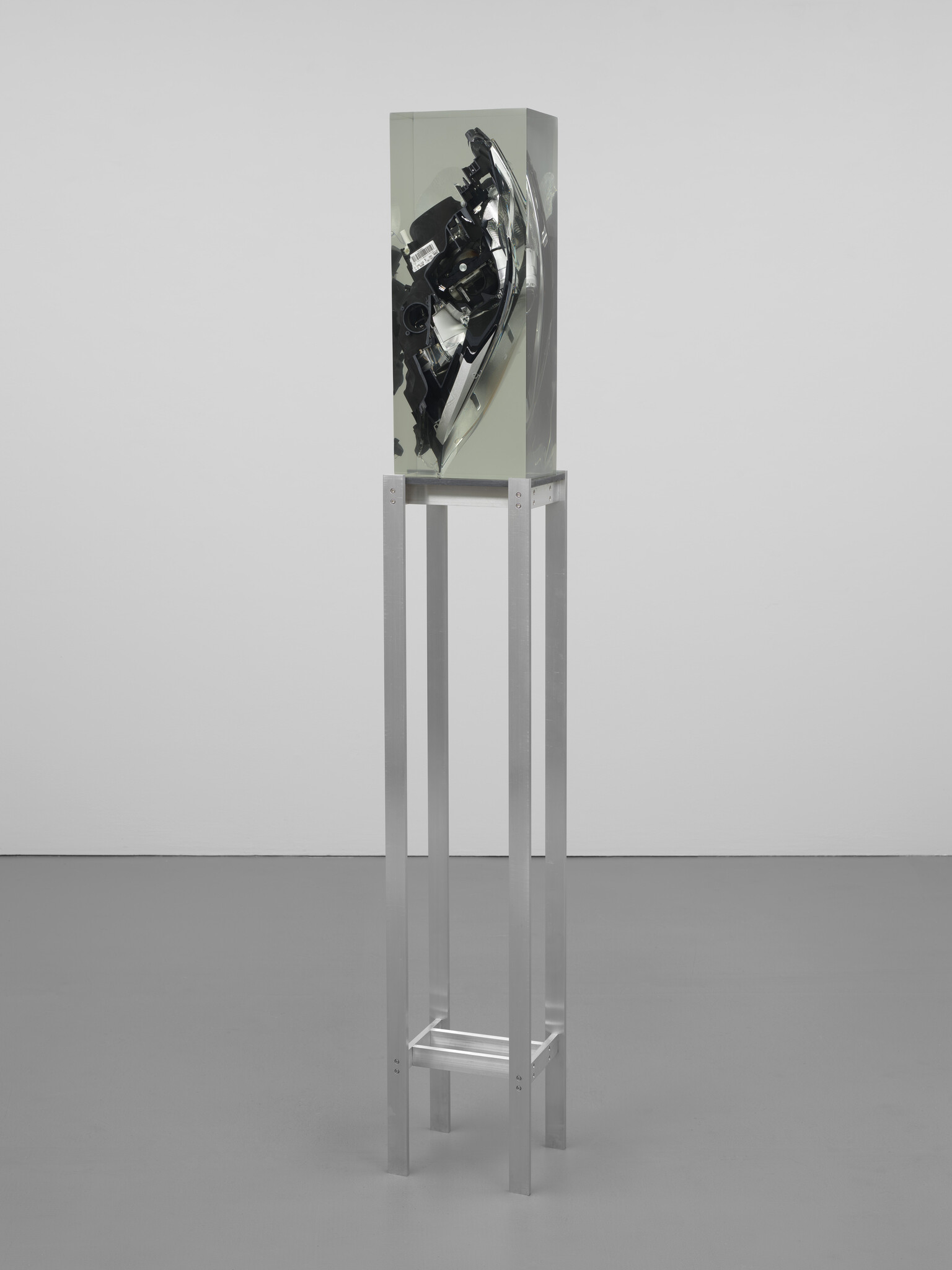 A tall metal stand supports a clear rectangular block encasing a car headlight assembly.