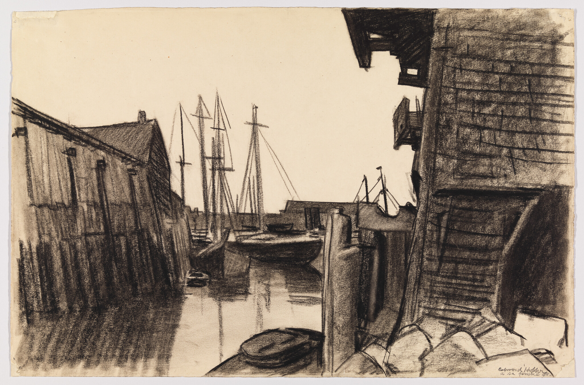 Boats and tall masts sit moored between wooden docks and buildings in a quiet harbor.