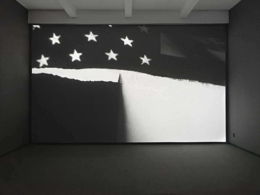 A large black-and-white projection shows a torn flag-like image with stars across the top.