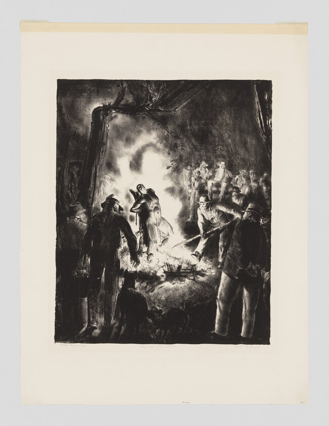 A crowd gathers around a large night fire as several men tend the flames and watch.
