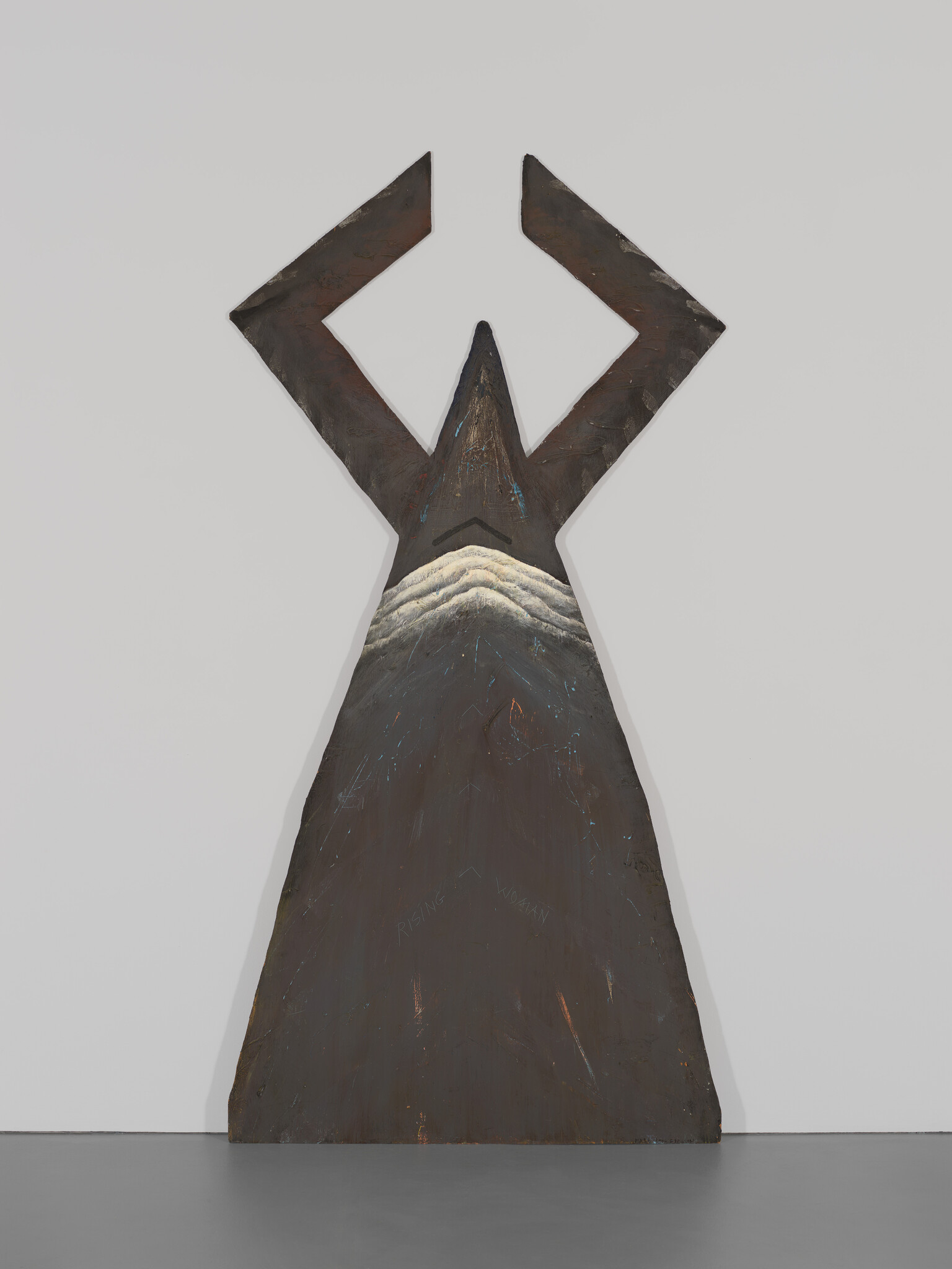 Large, dark, abstract sculpture shaped like a figure with raised arms; the words "RISING WOMAN" are carved on it.